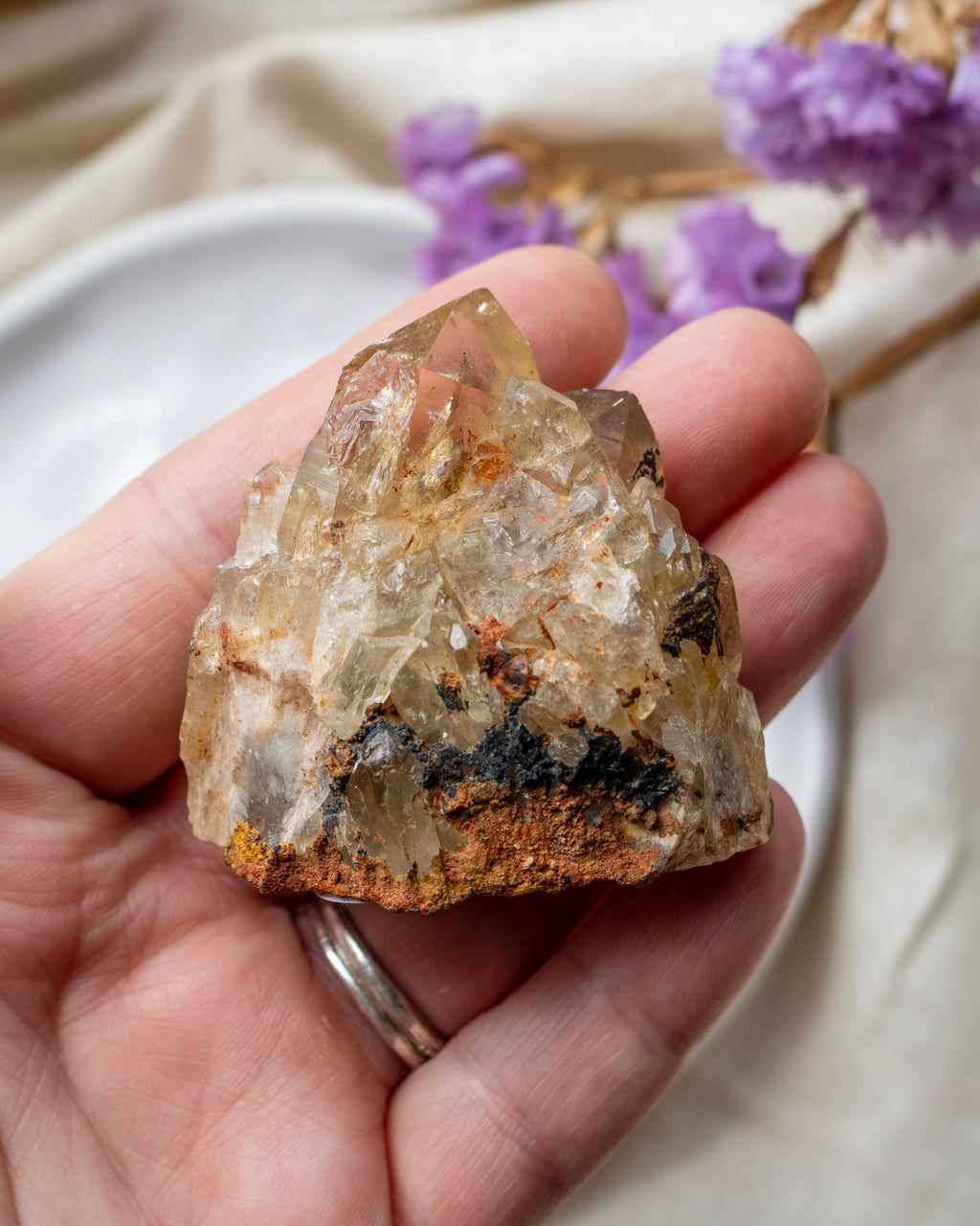 Hand holding a crystal rock with purple flowers in the background