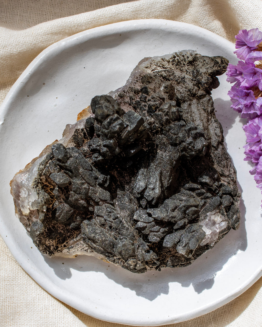 Mineral specimen on a white plate with purple flowers