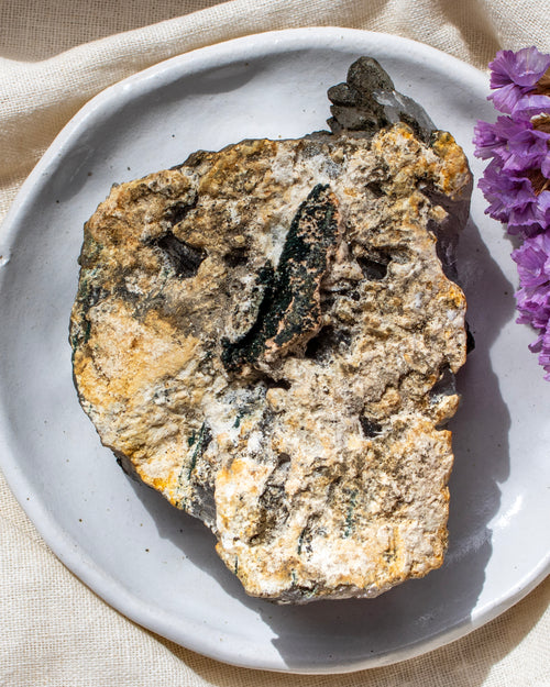 Mineral specimen on a white plate with purple flowers
