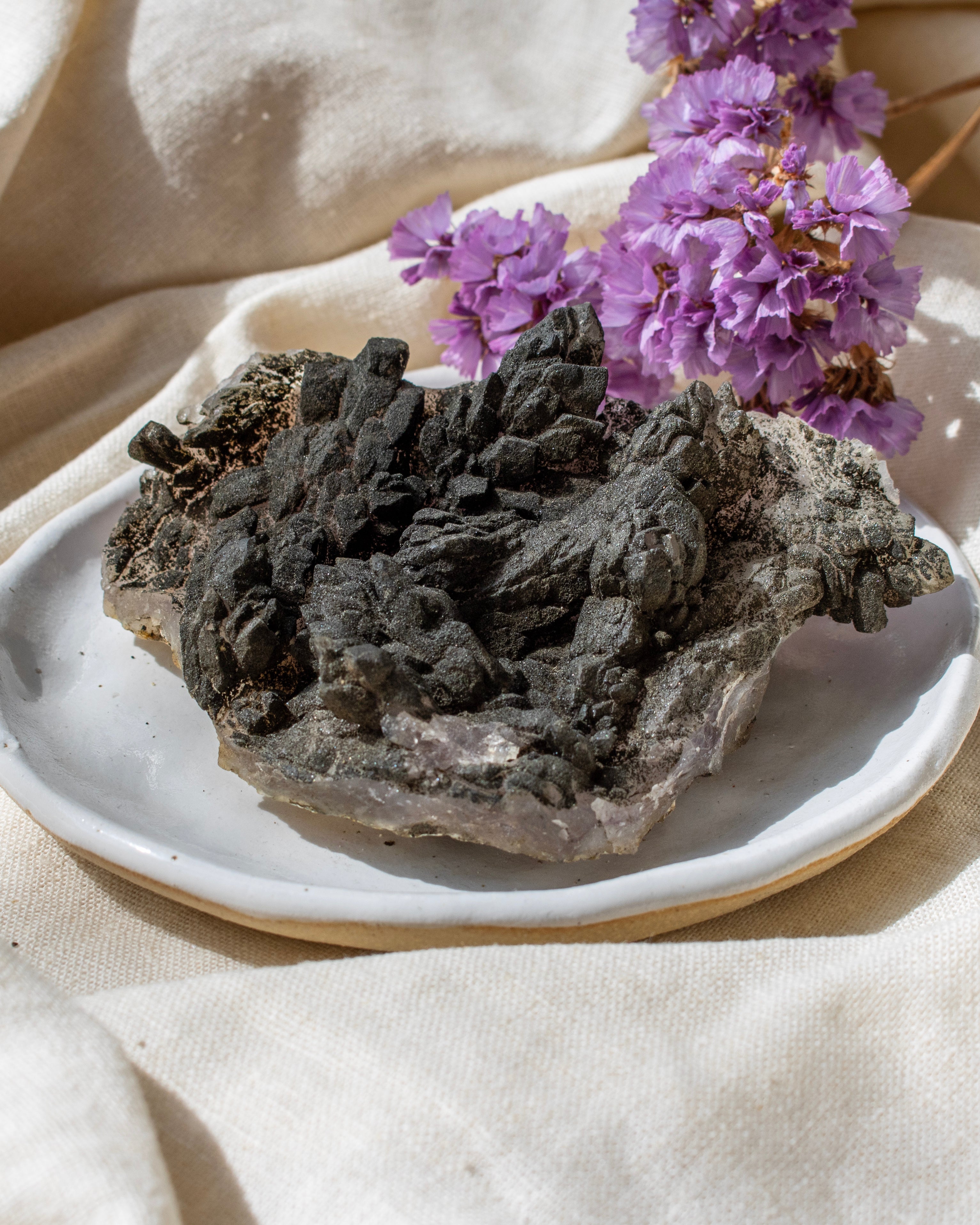 Mineral specimen on a white plate with purple flowers