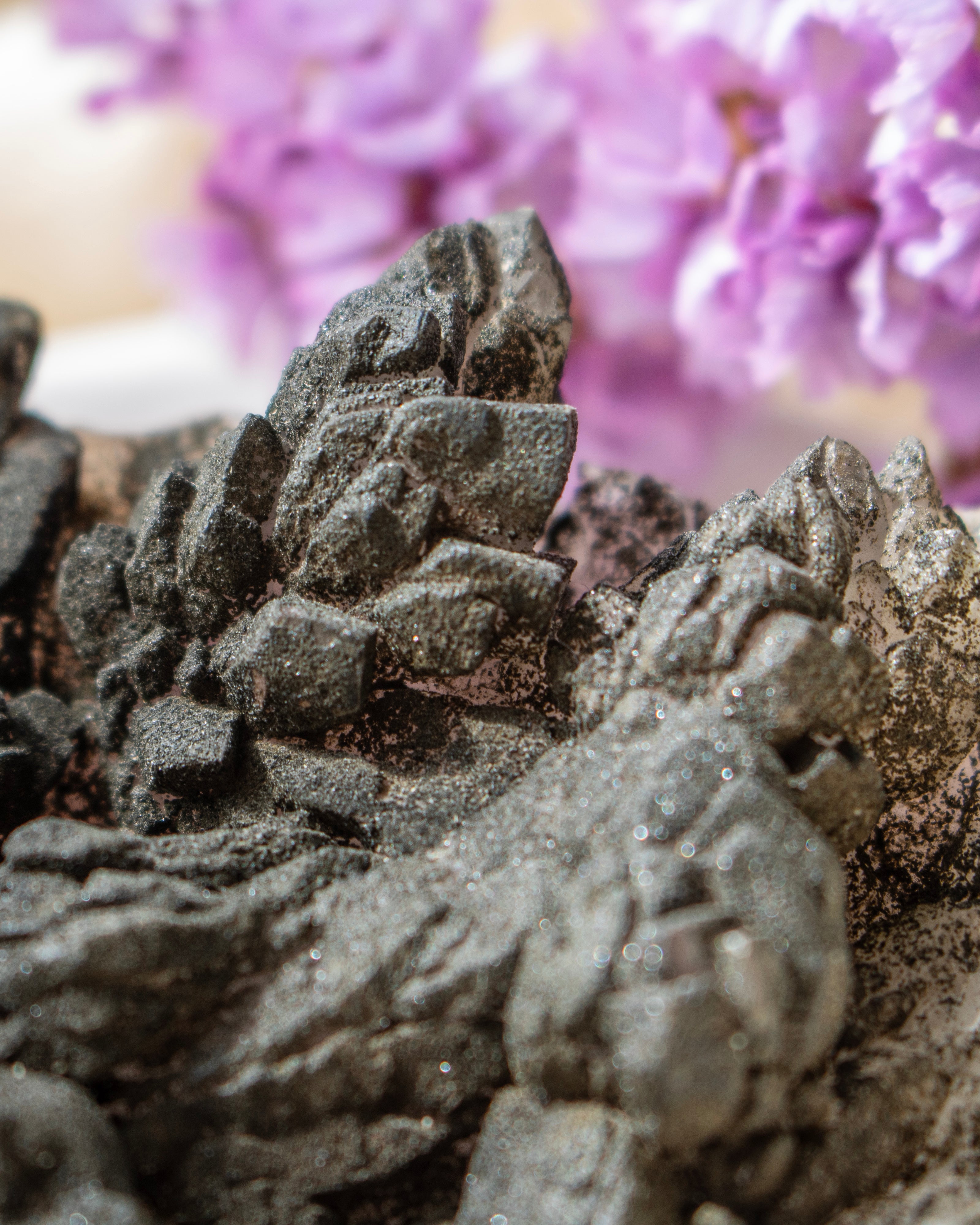 Close-up of dark mineral crystal with blurry background of purple flowers