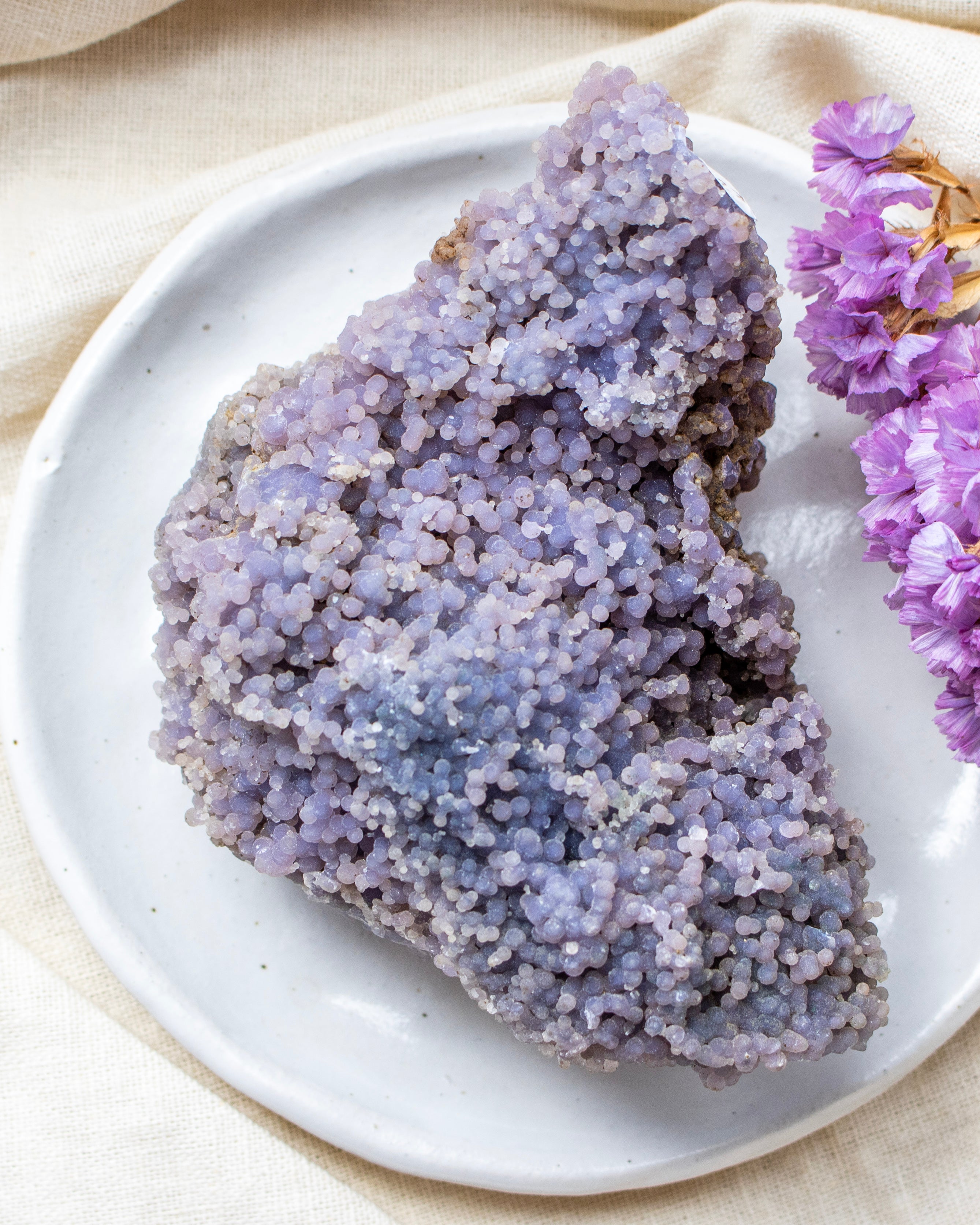 Purple crystal rock on a white plate with purple flowers