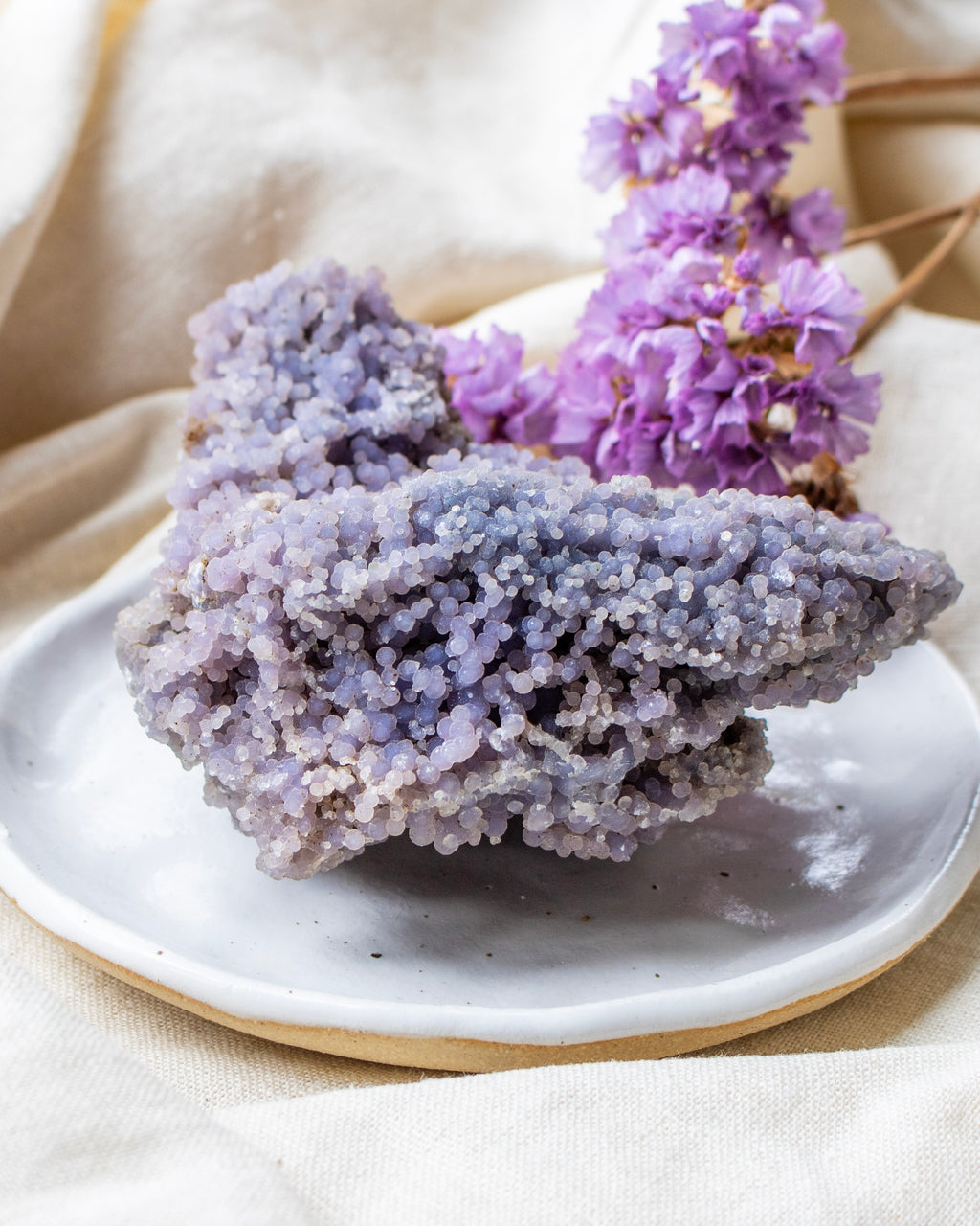 Purple crystal rock on a white plate with purple flowers in the background
