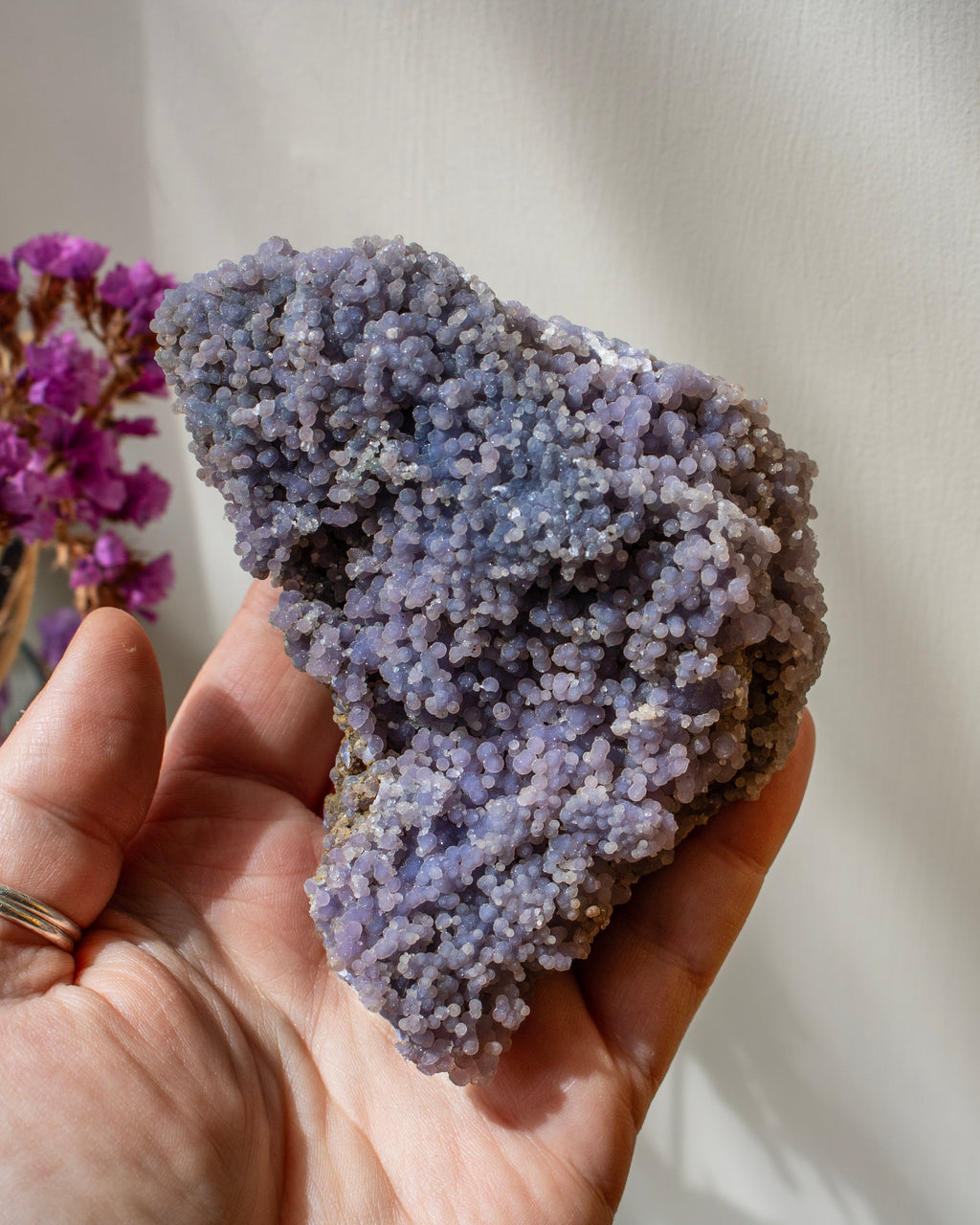 Hand holding a purple crystal rock with blurred purple flowers in the background