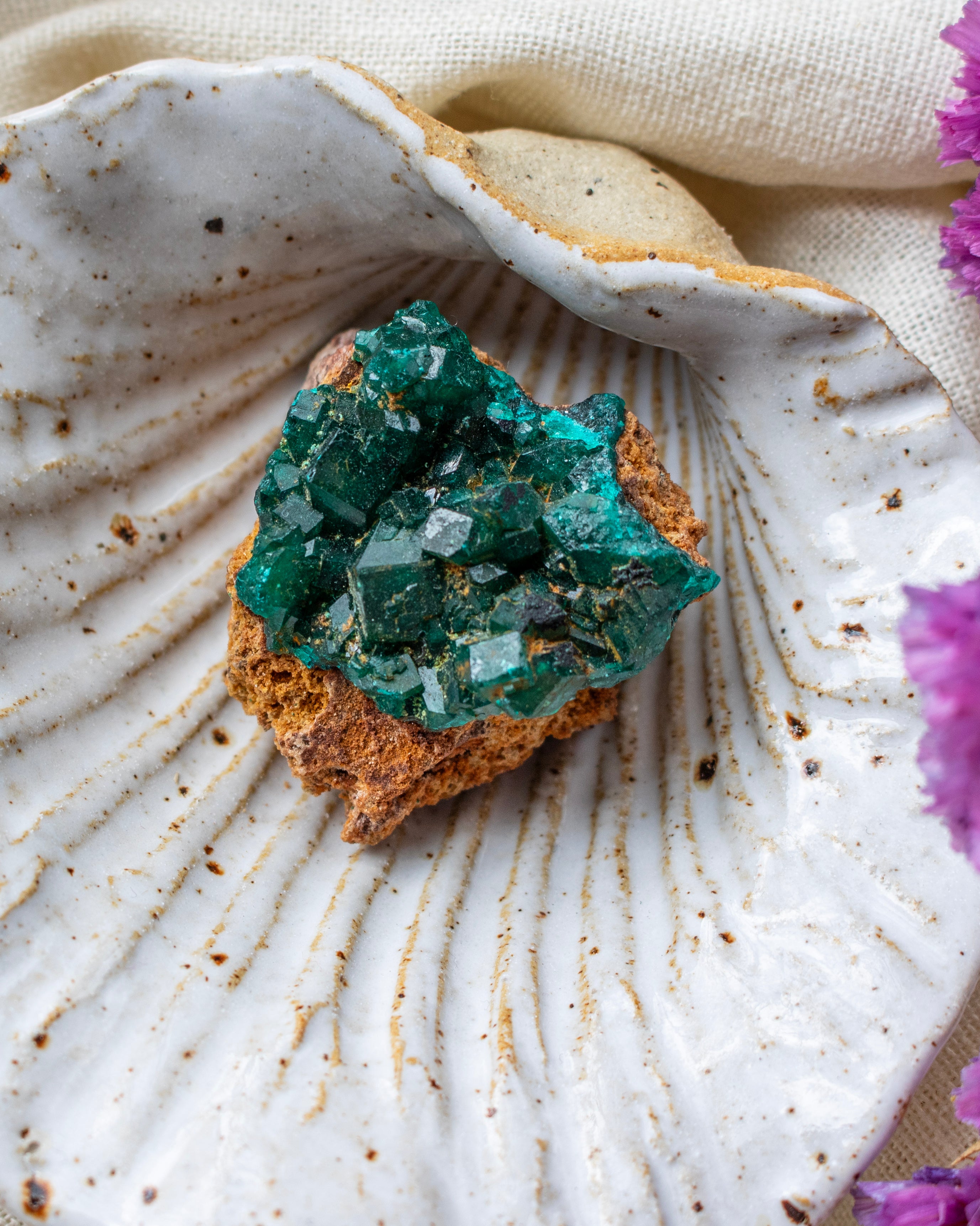 Green crystal cluster on a textured white surface with purple flowers