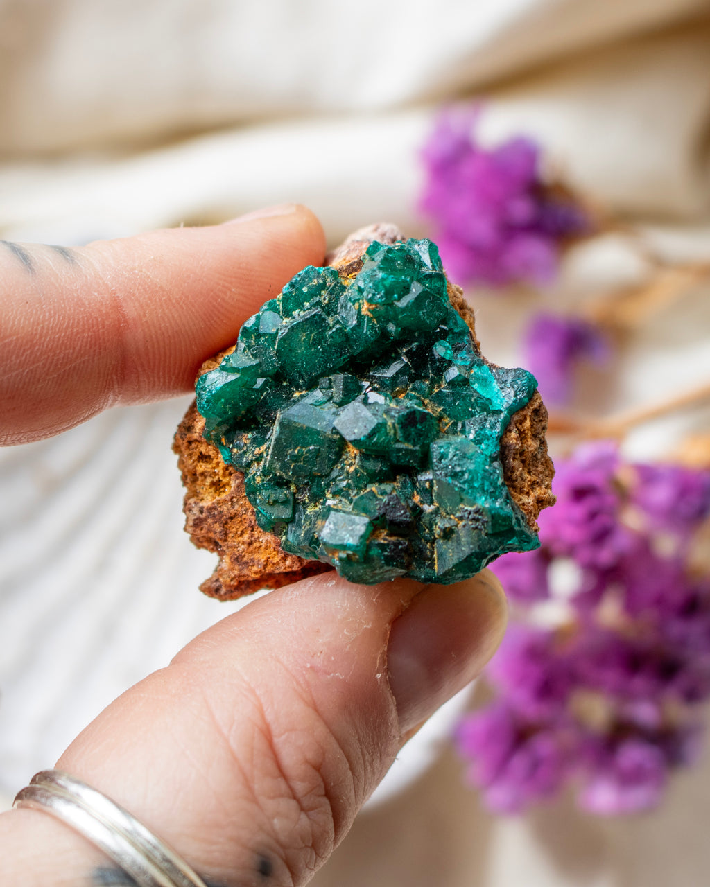 Hand holding a green crystal cluster with blurred purple flowers in the background
