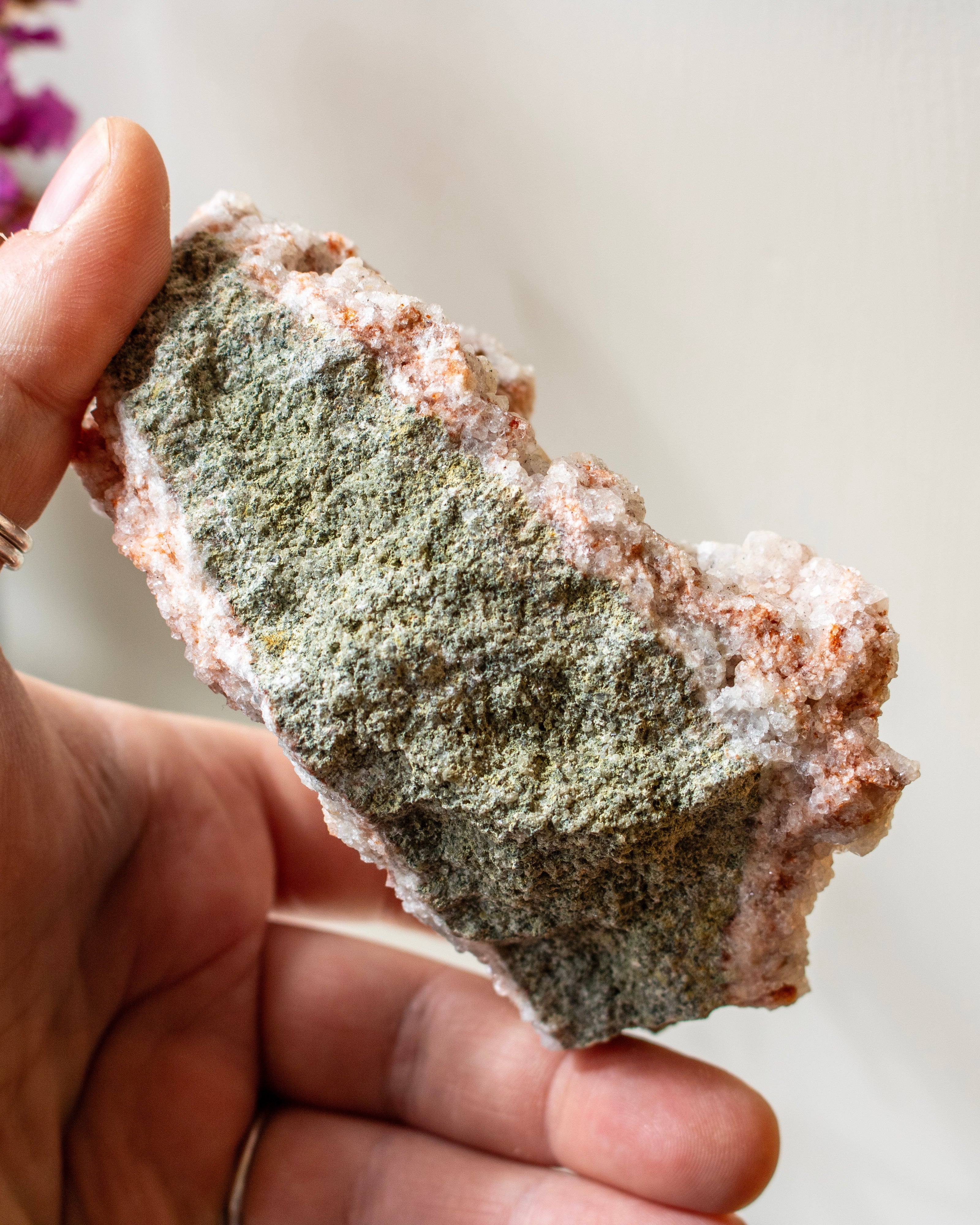 Hand holding a piece of rock with green mineral deposits against a blurred background