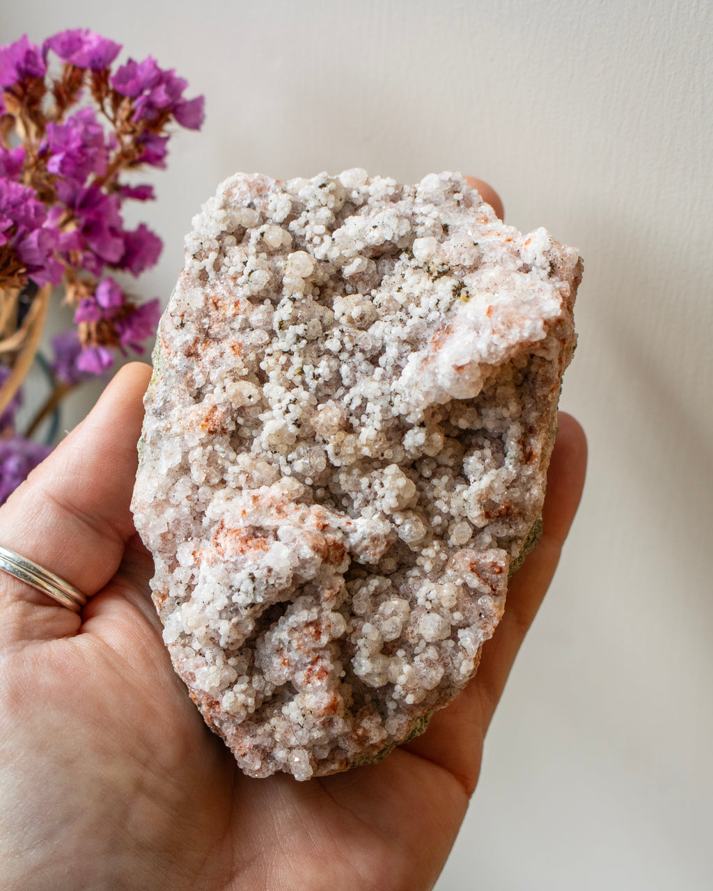 Hand holding a large crystal rock with a blurred purple flower in the background