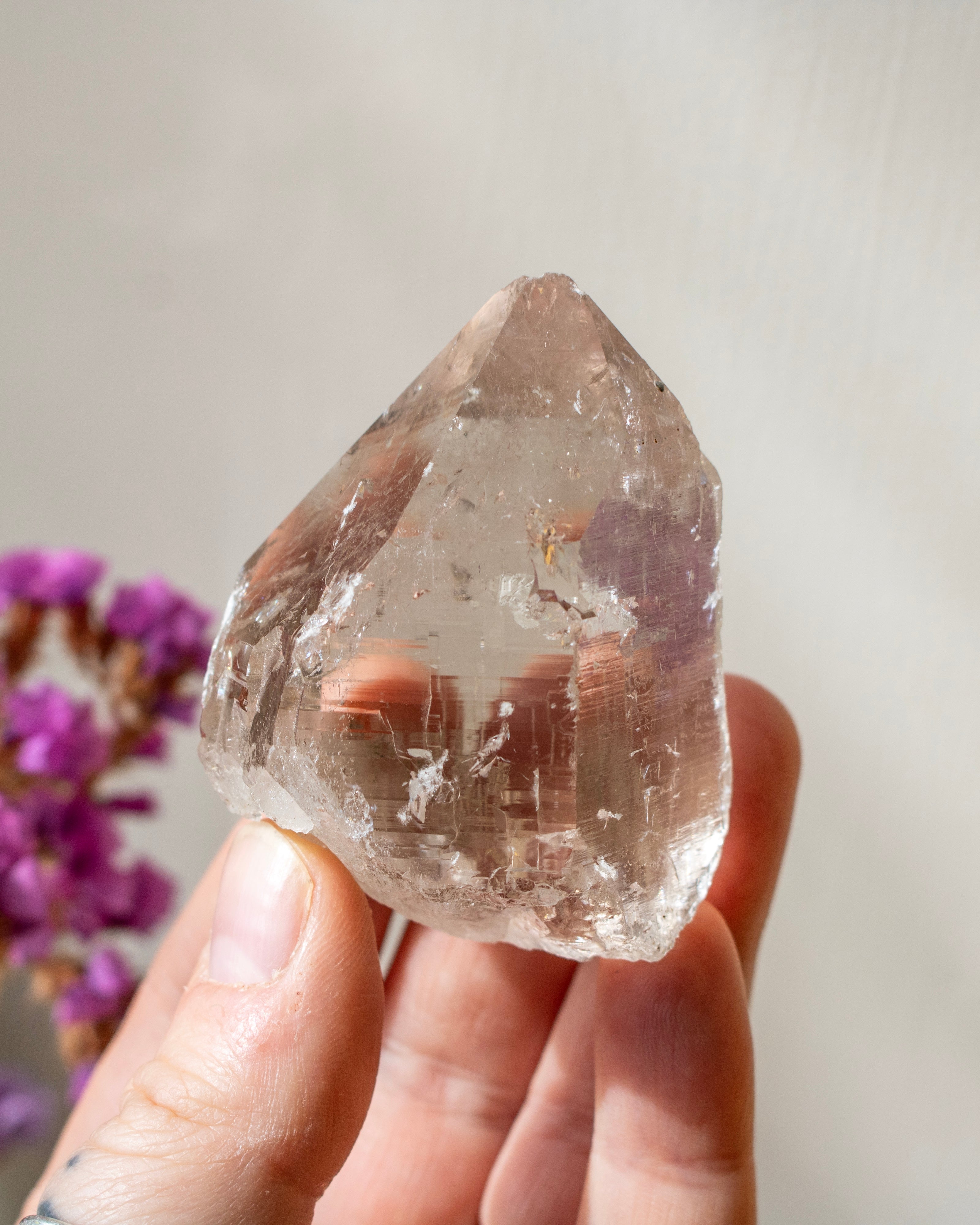 Hand holding a clear crystal with a blurred background of pink flowers