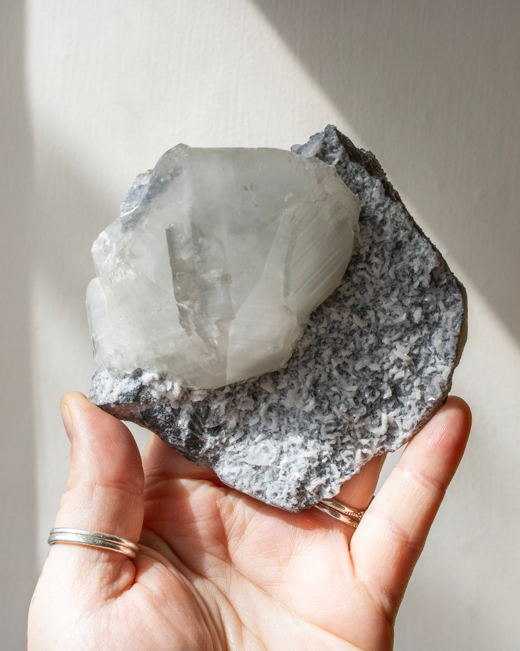 Hand holding a large crystal with a light-colored interior and dark exterior against a neutral background