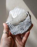 Hand holding a crystal rock with a white mineral formation against a neutral background