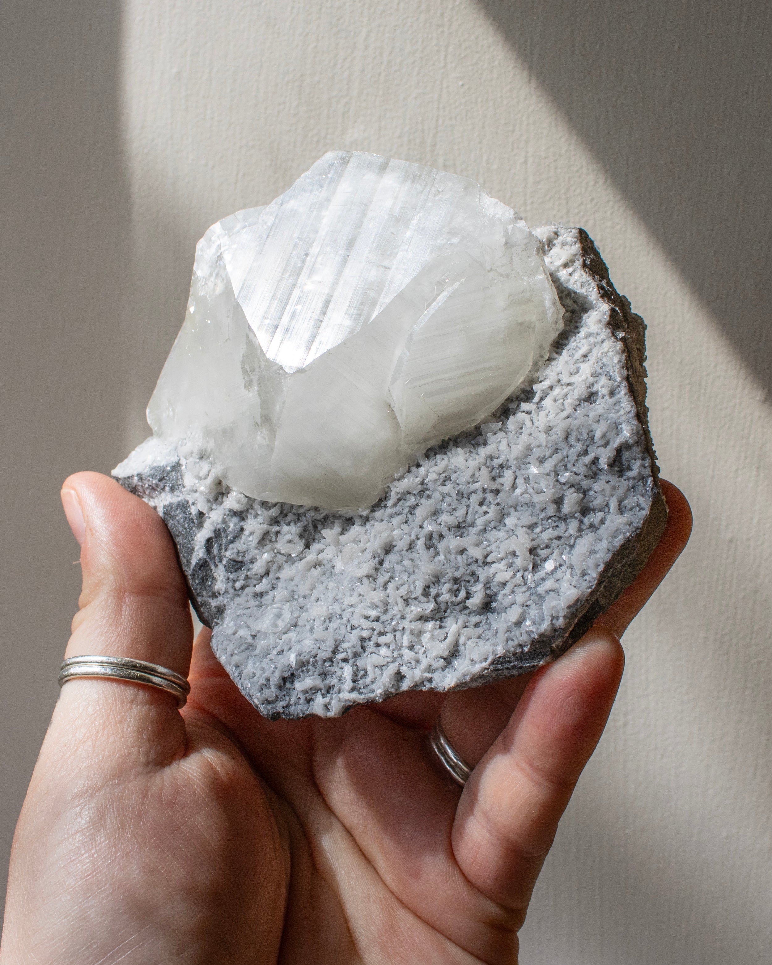 Hand holding a crystal rock with a white mineral formation against a neutral background
