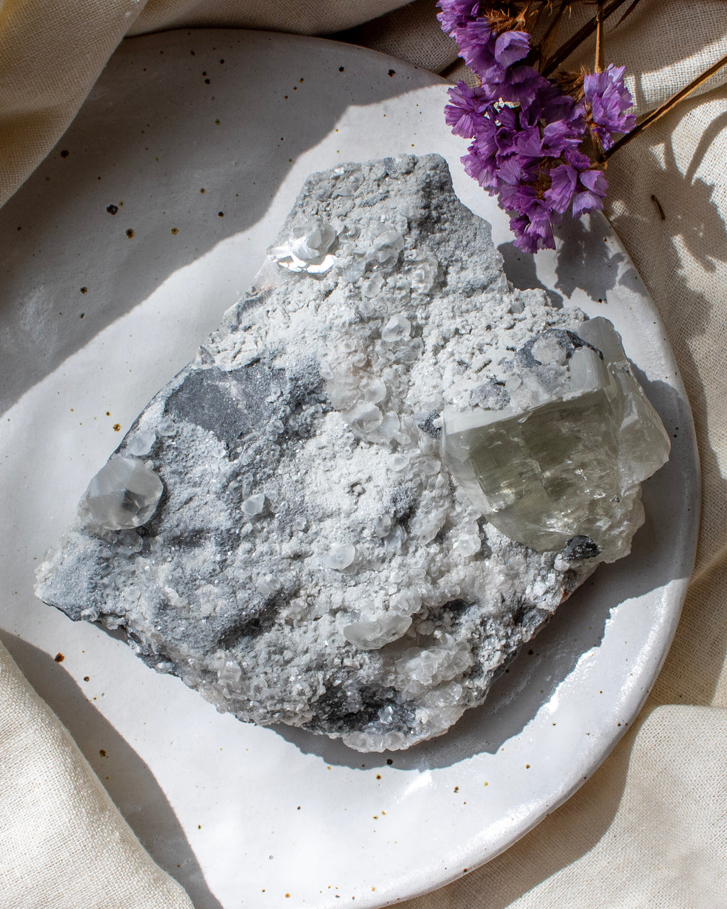 Mineral specimen on a speckled ceramic plate with purple flowers