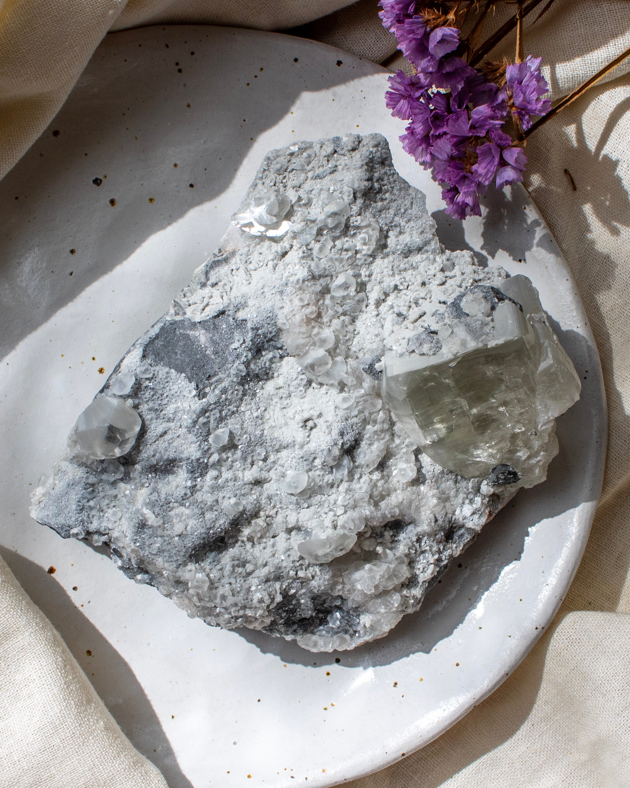 Mineral specimen on a speckled ceramic plate with purple flowers