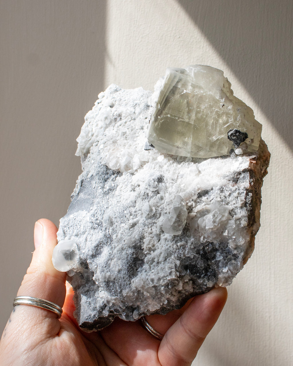 Hand holding a crystal rock with a clear mineral on a neutral background