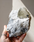 Hand holding a crystal rock with a clear mineral on a neutral background
