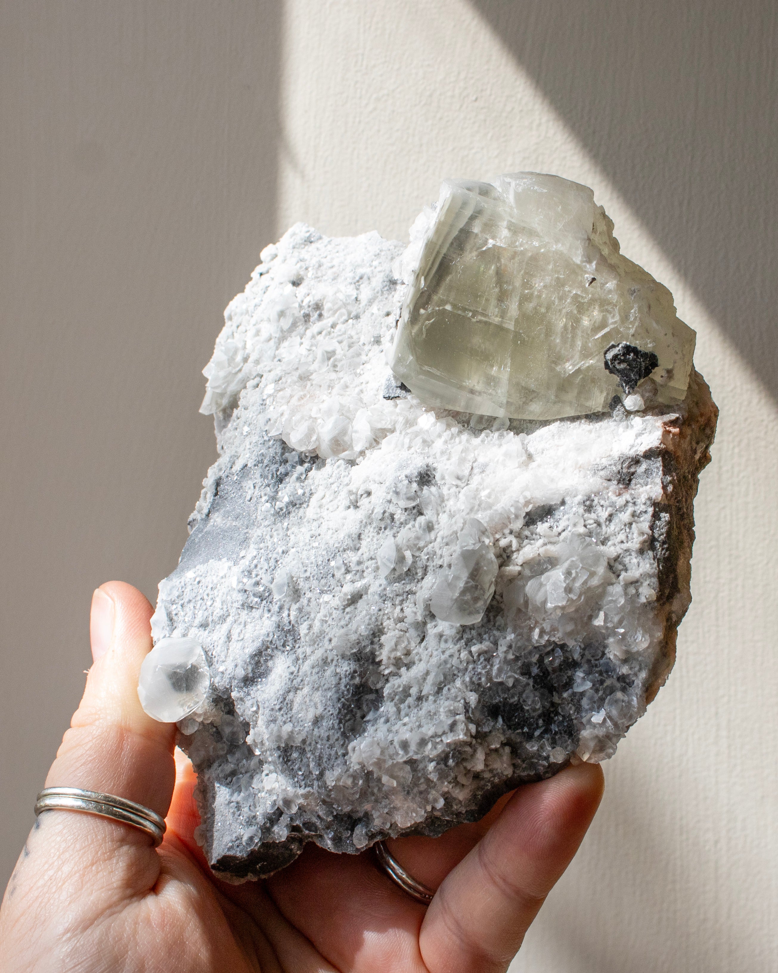Hand holding a crystal rock with a clear mineral on a neutral background