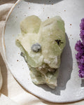 Mineral specimen on a speckled ceramic plate with a purple flower