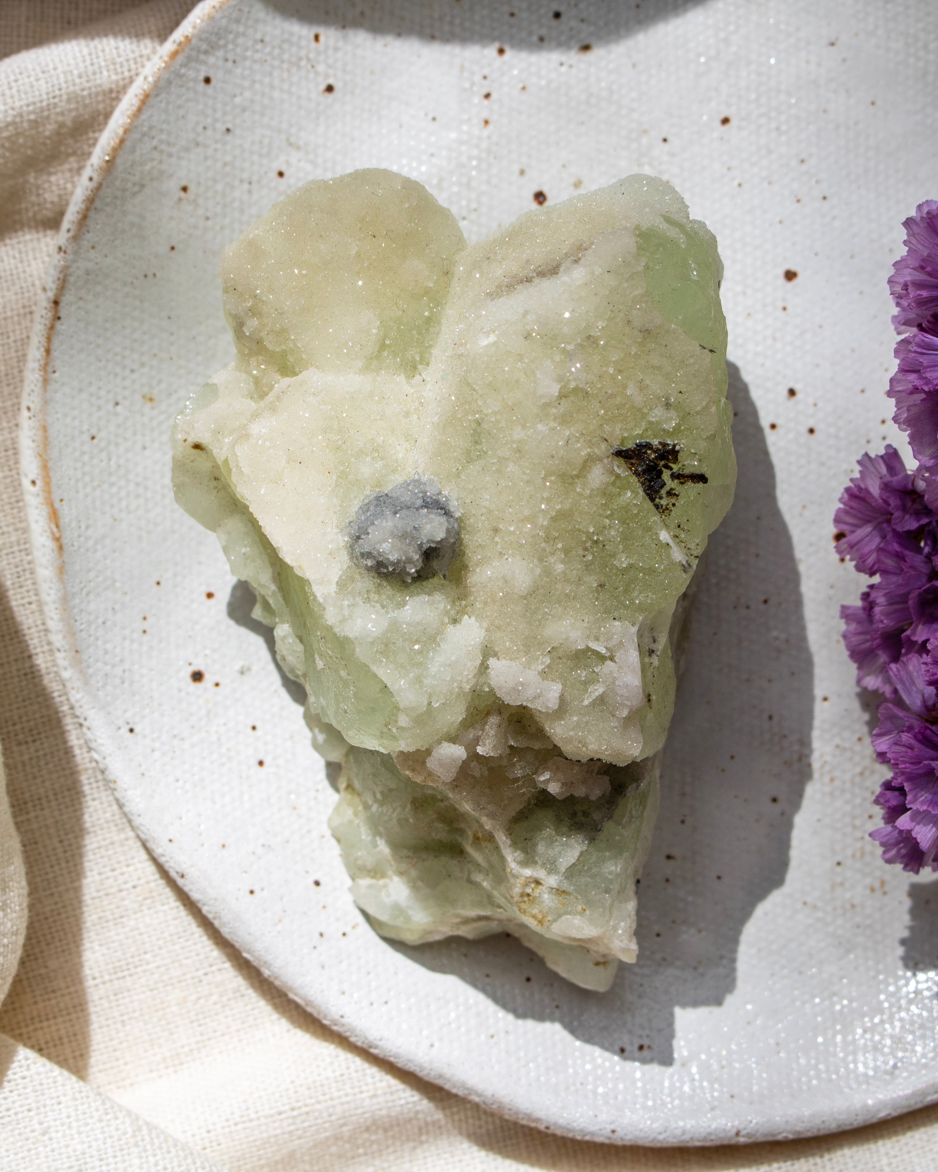 Mineral specimen on a speckled ceramic plate with a purple flower