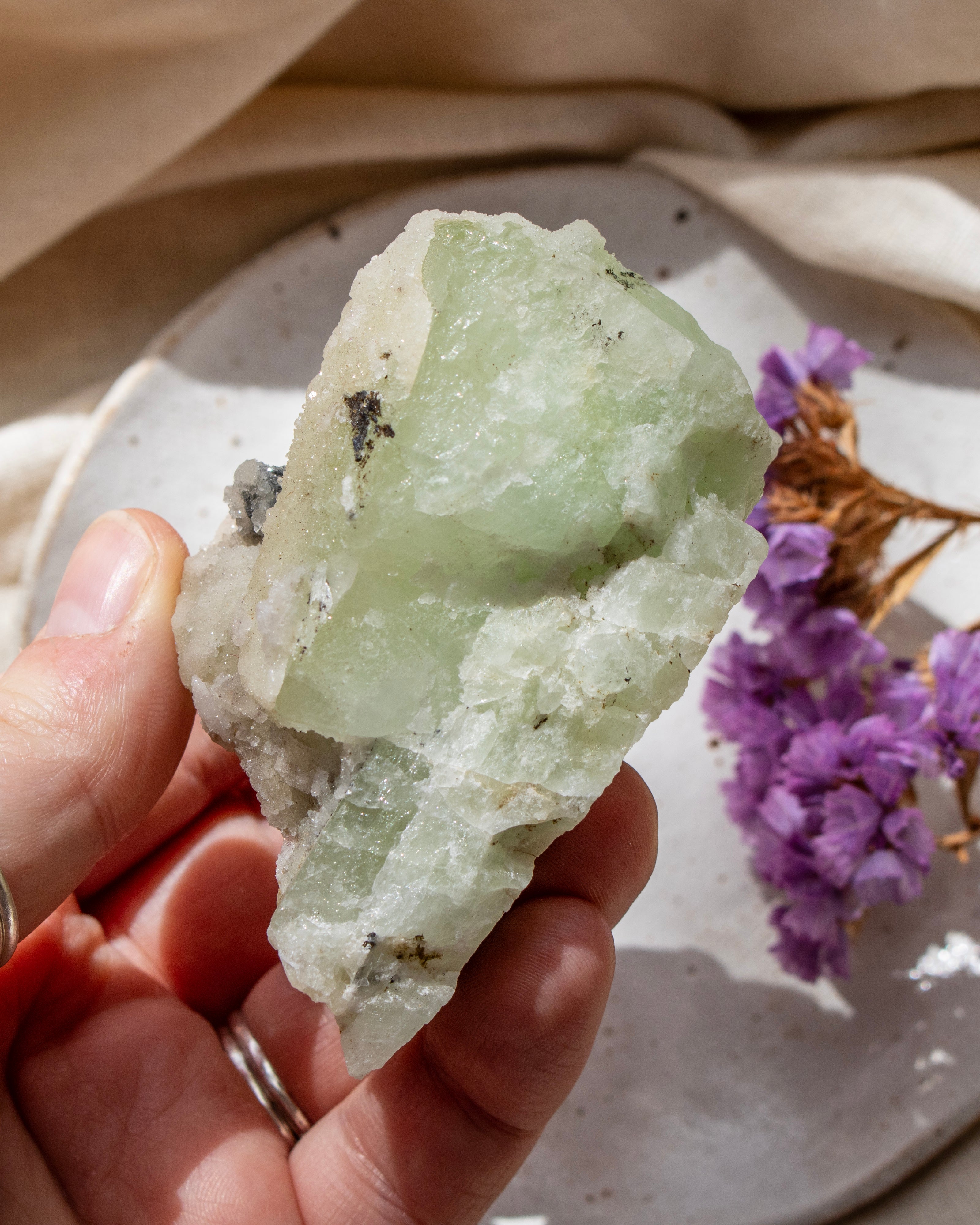Hand holding a green crystal with purple flowers and beige fabric in the background