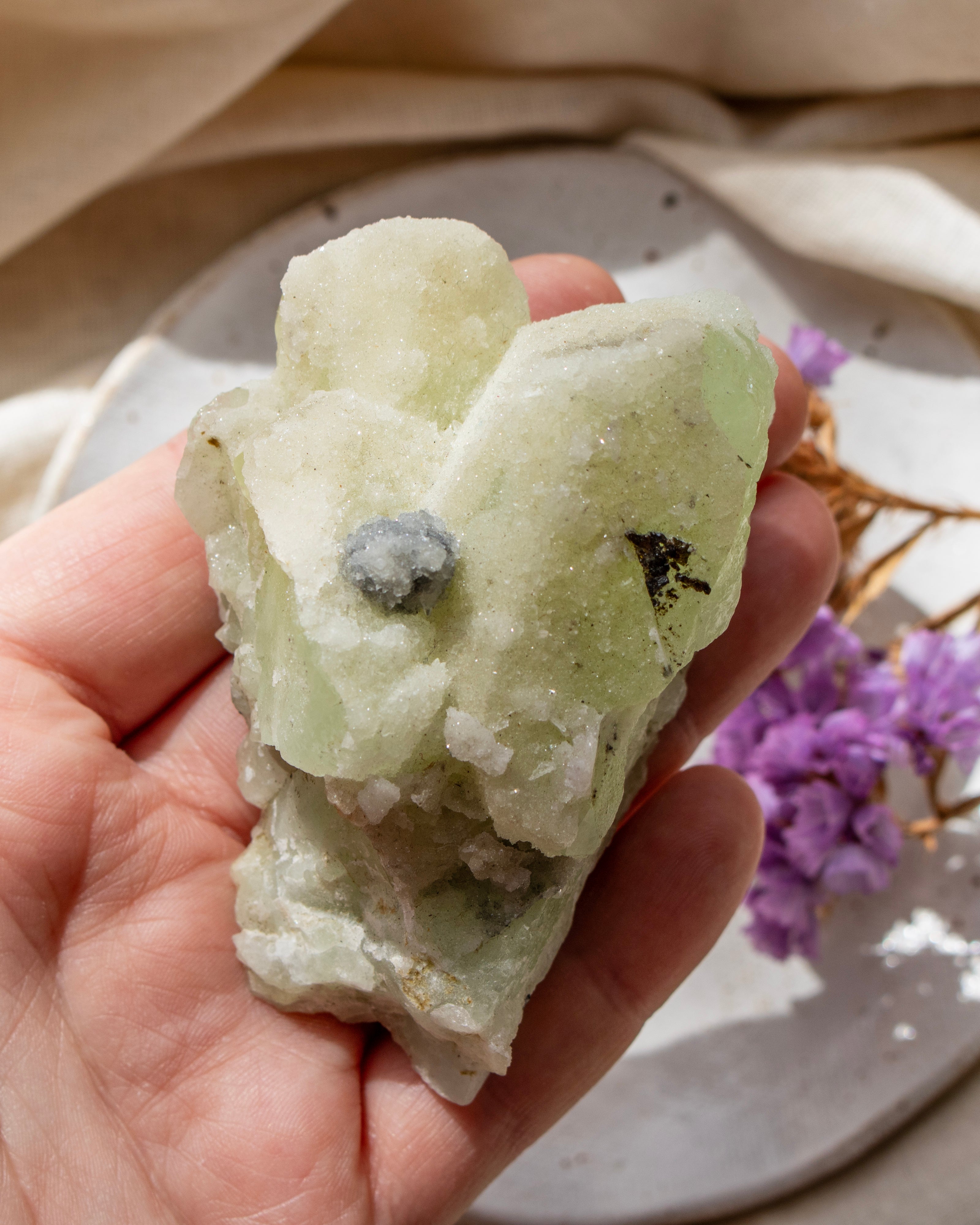 Hand holding a green crystal with a beige background