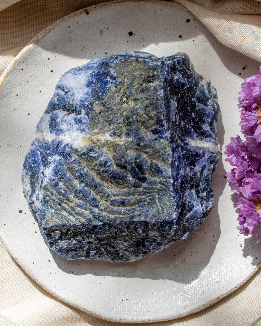 Blue stone on a textured white plate with purple flowers