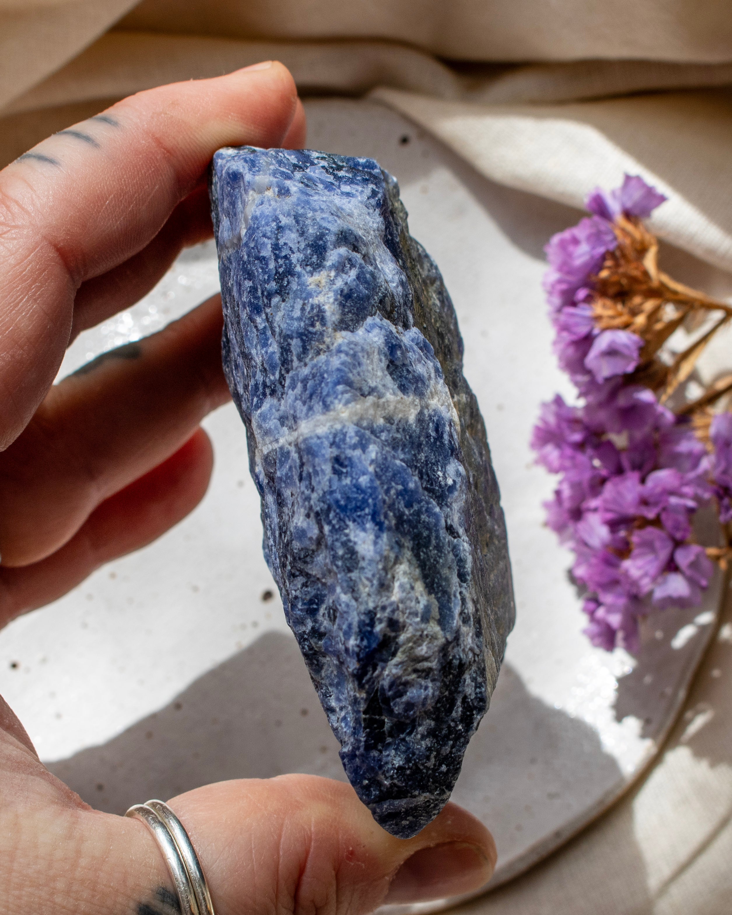 Hand holding a blue stone with purple flowers on a light surface