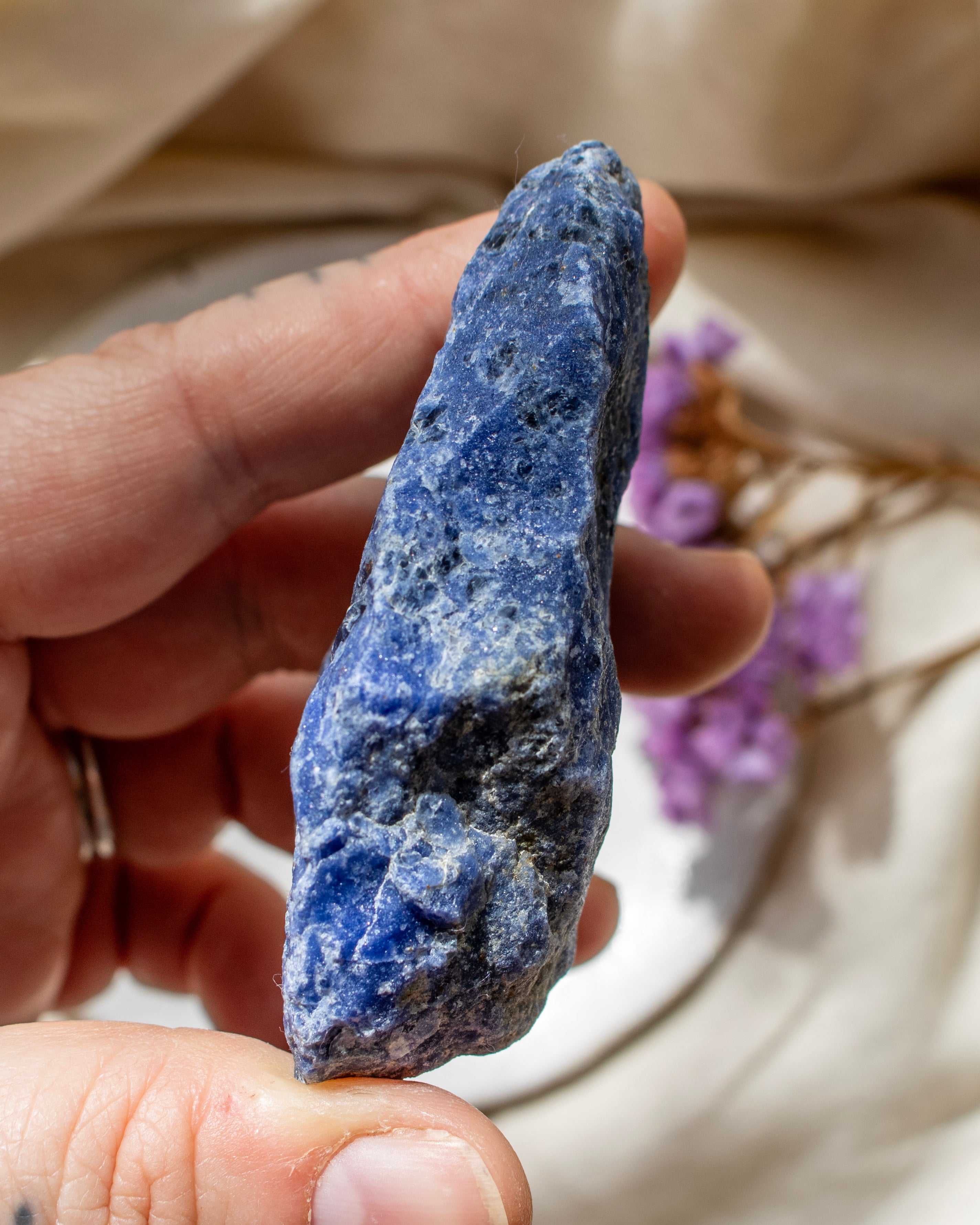 Hand holding a blue stone with a blurred natural background