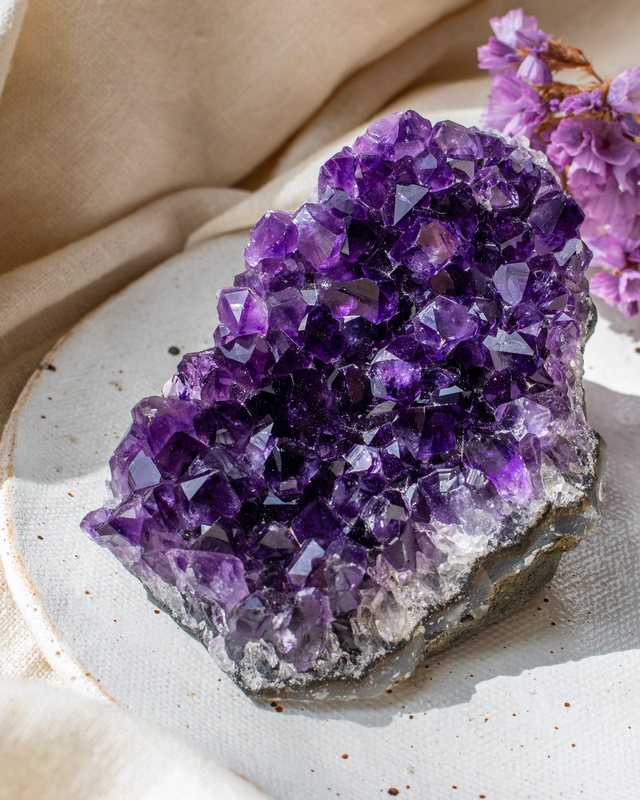 Amethyst crystal cluster on a white surface with a beige cloth background