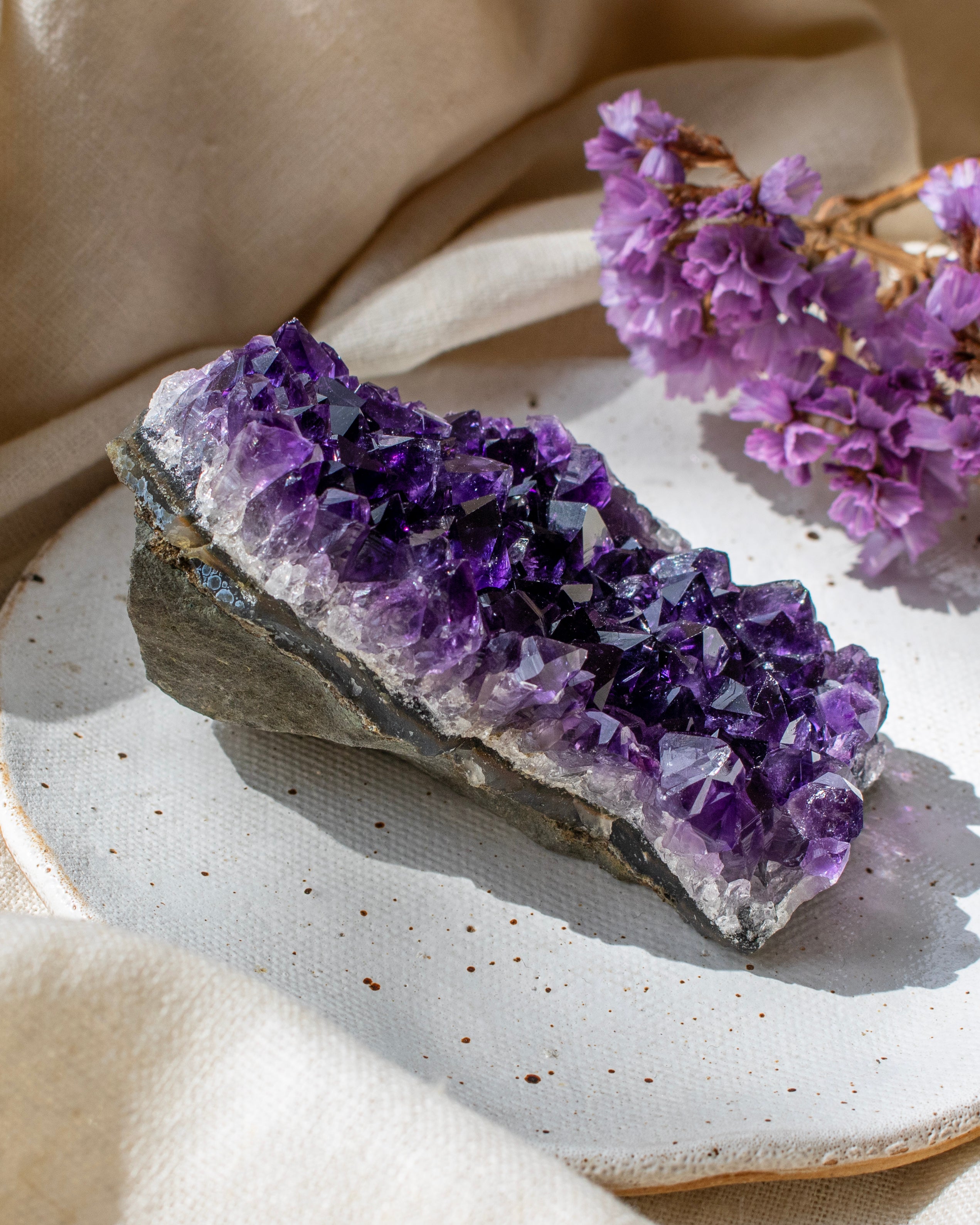 Amethyst crystal on a ceramic plate with purple flowers in the background