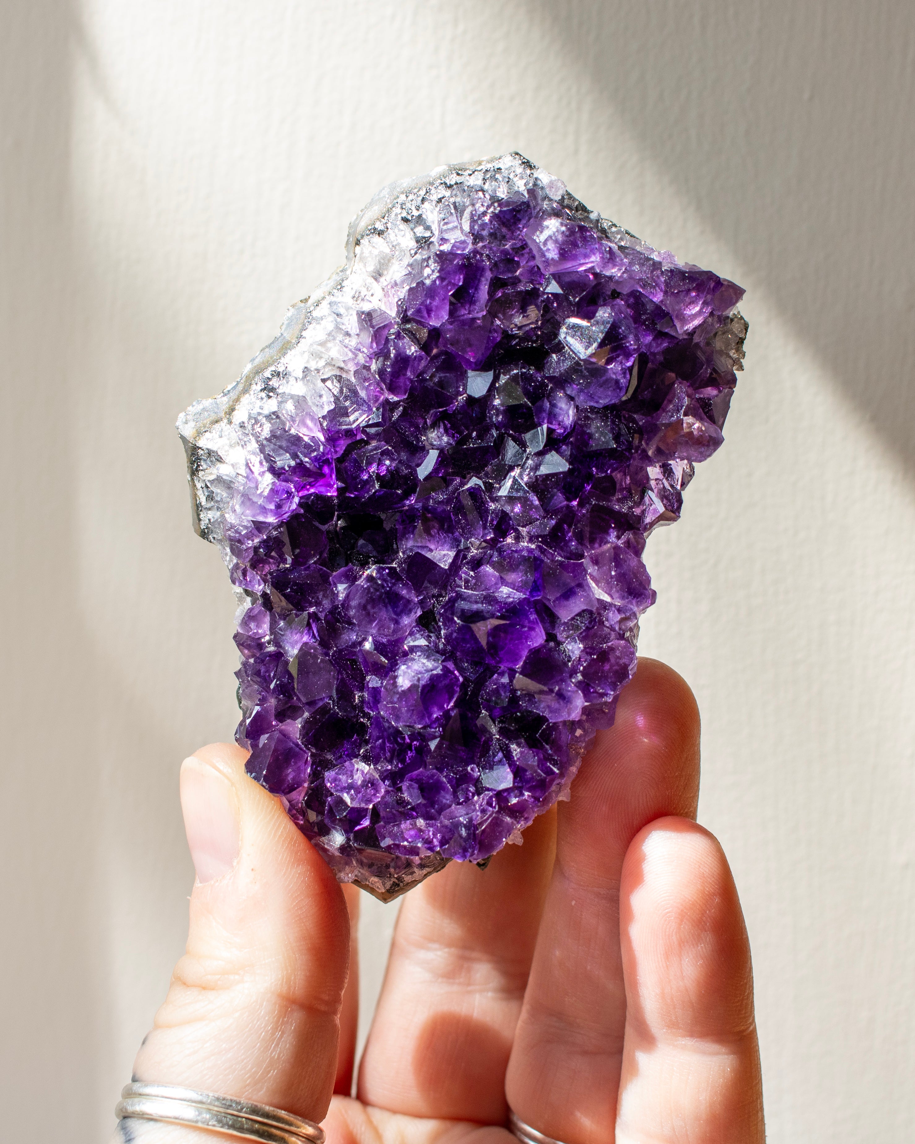 Hand holding a large purple crystal against a neutral background