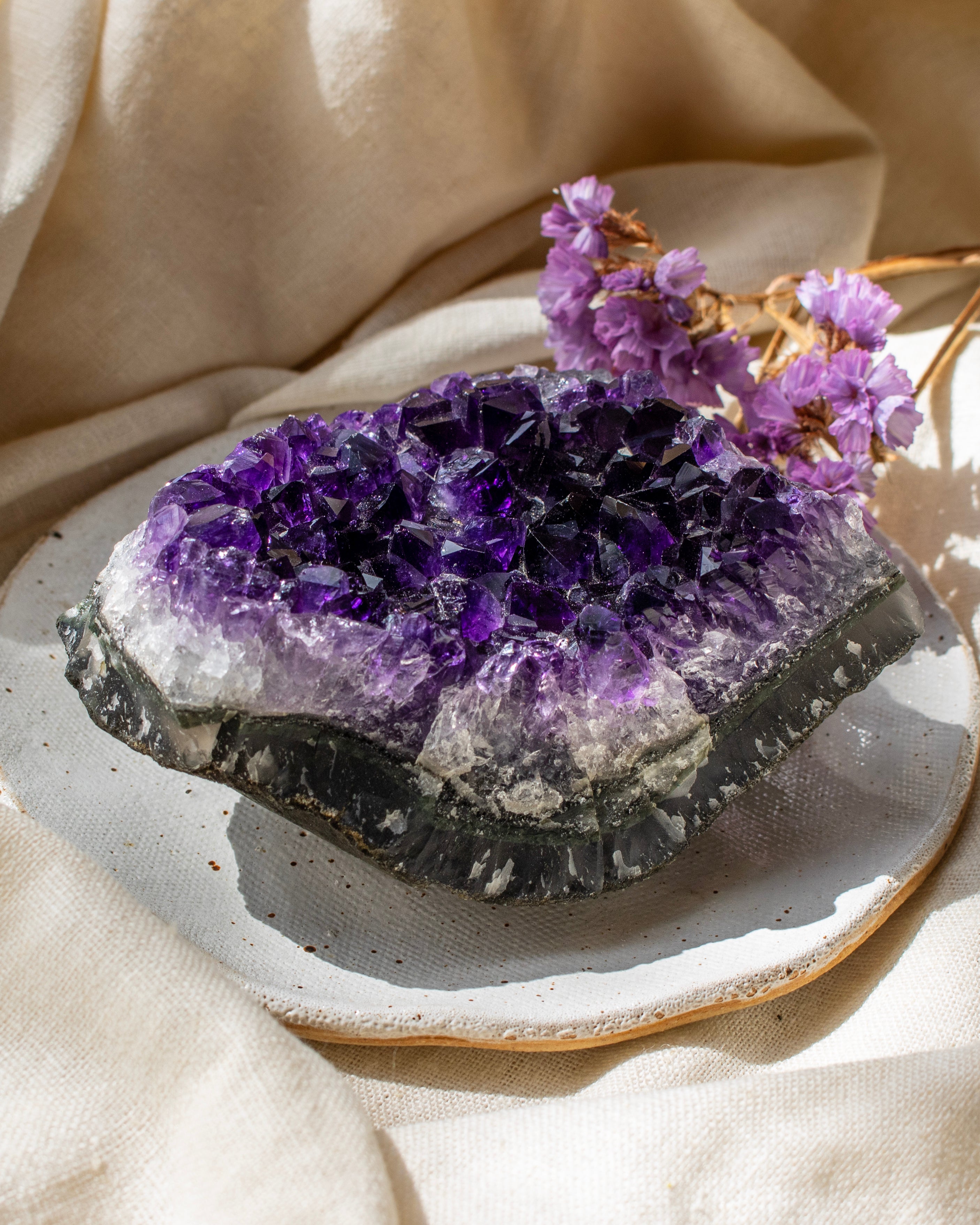Amethyst crystal on a ceramic plate with purple flowers