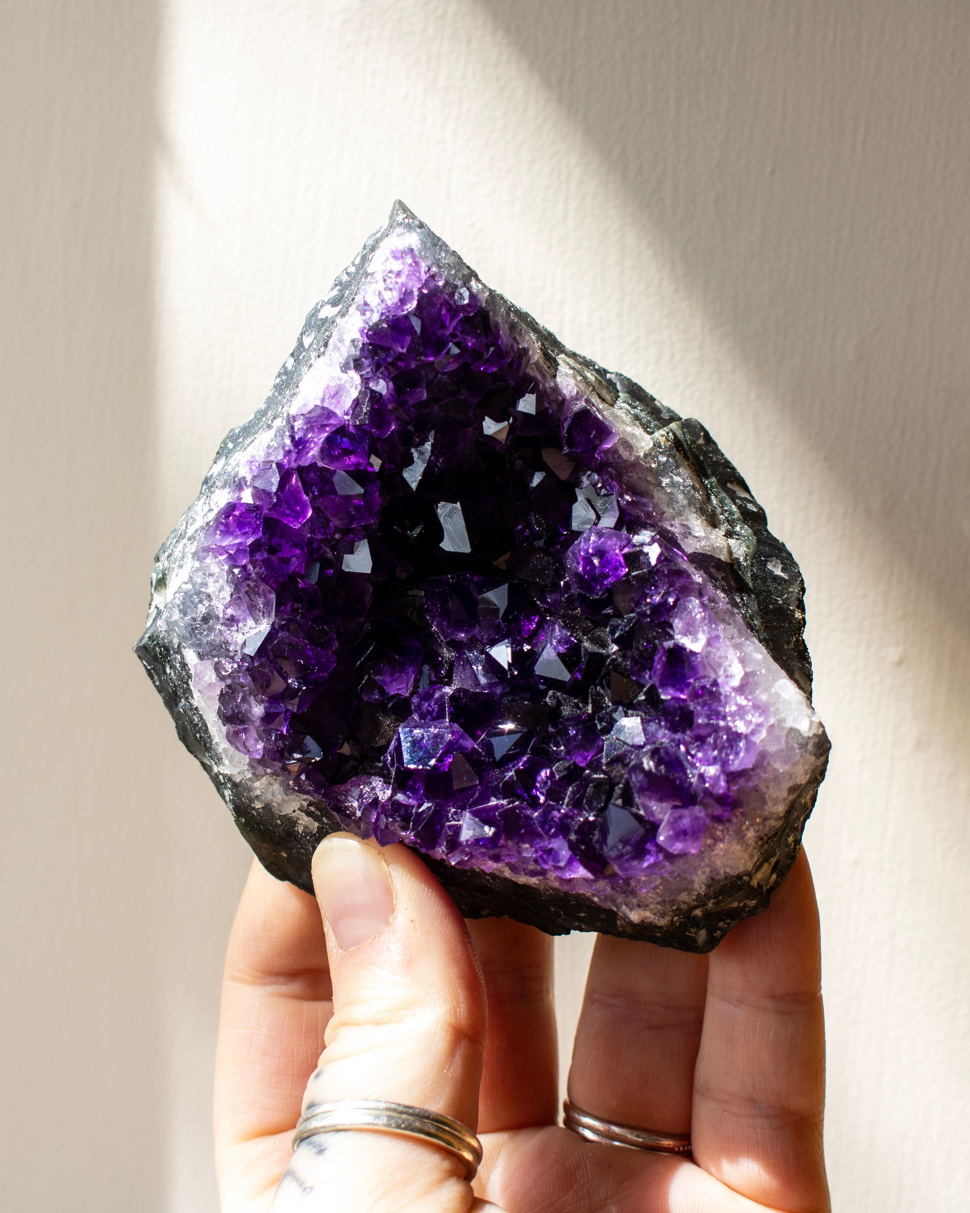 Amethyst crystal held in a hand against a neutral background