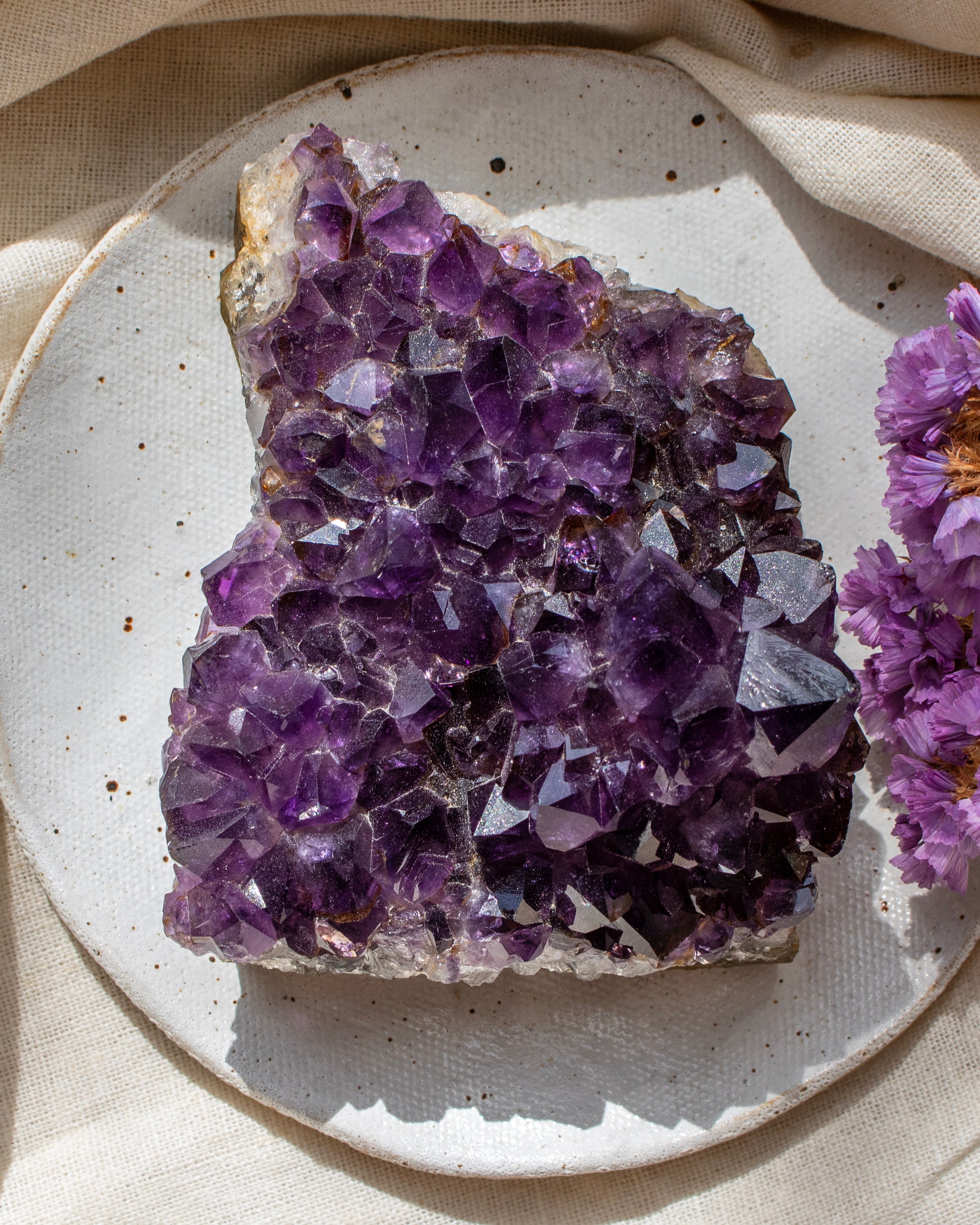 Amethyst crystal cluster on a ceramic plate with a beige cloth background