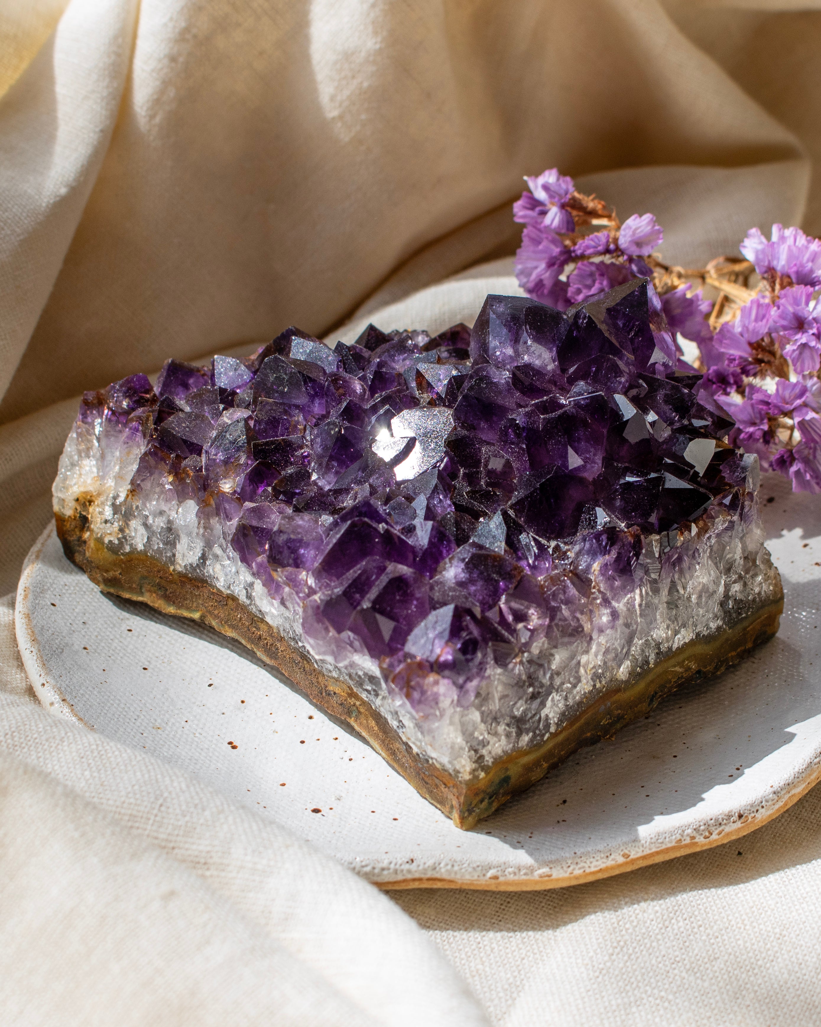 Amethyst crystal cluster on a ceramic plate with a beige cloth background