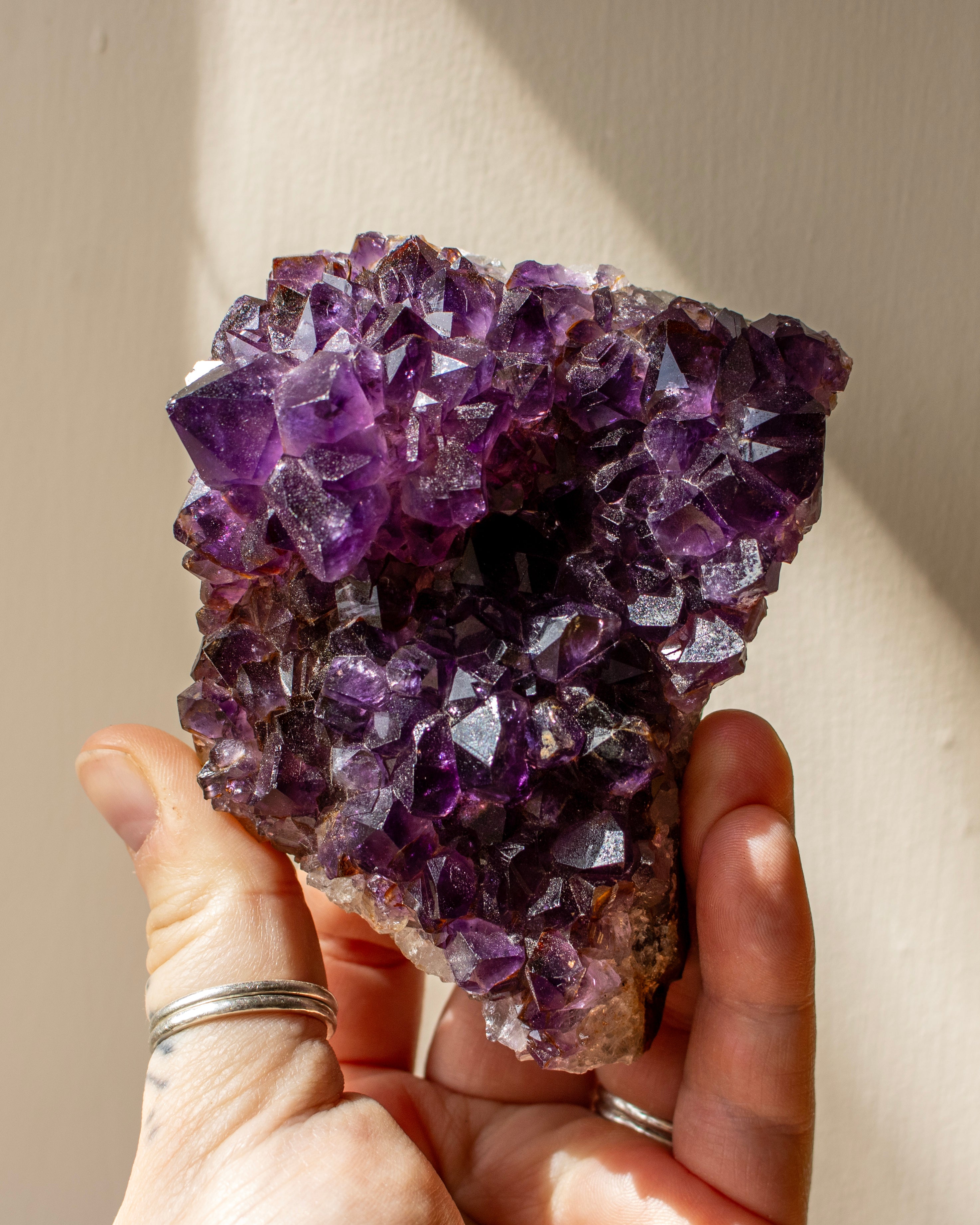 an amethyst crystal being held in a hand in front of a neutral background