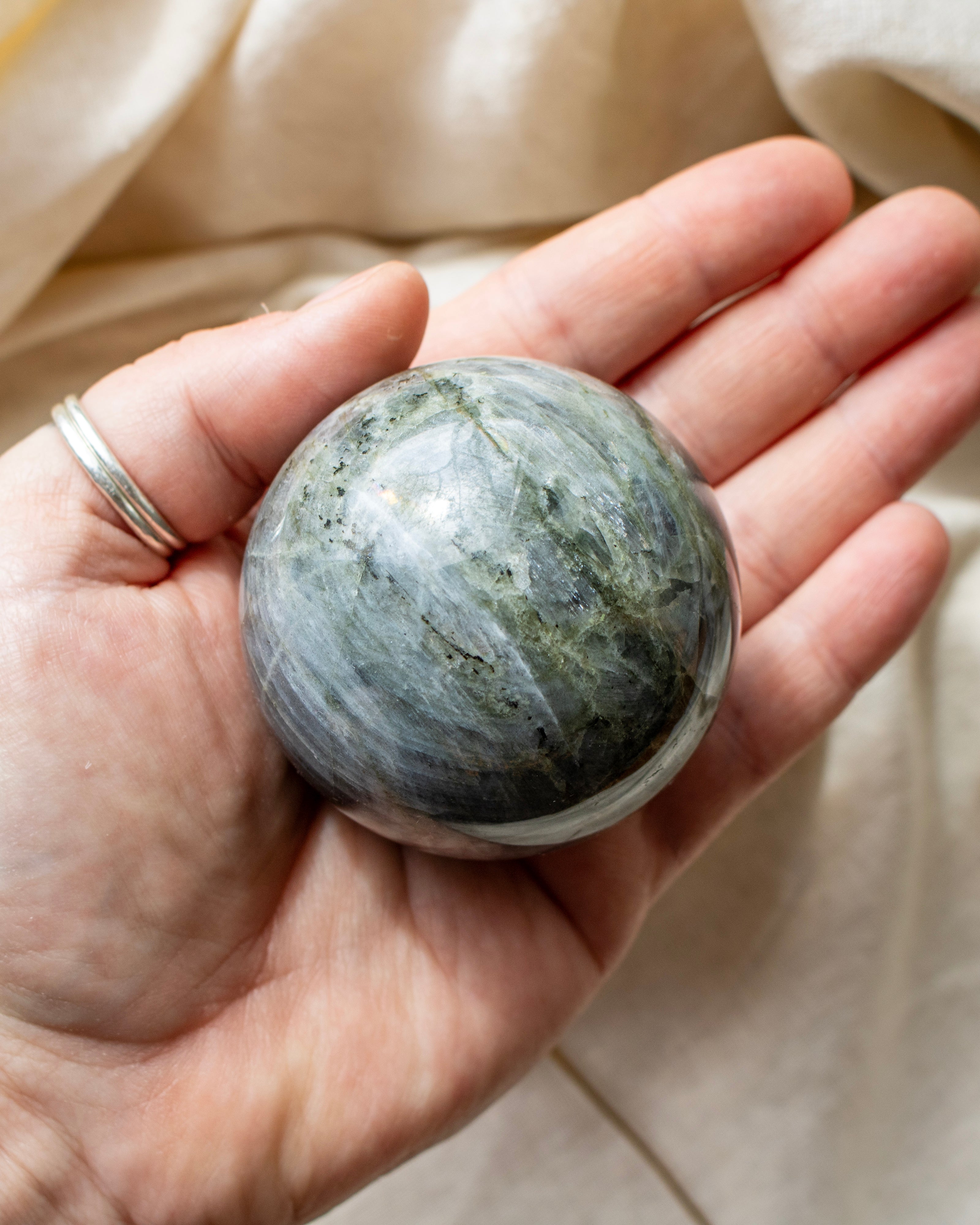 Hand holding a greenish-blue stone against a beige fabric background