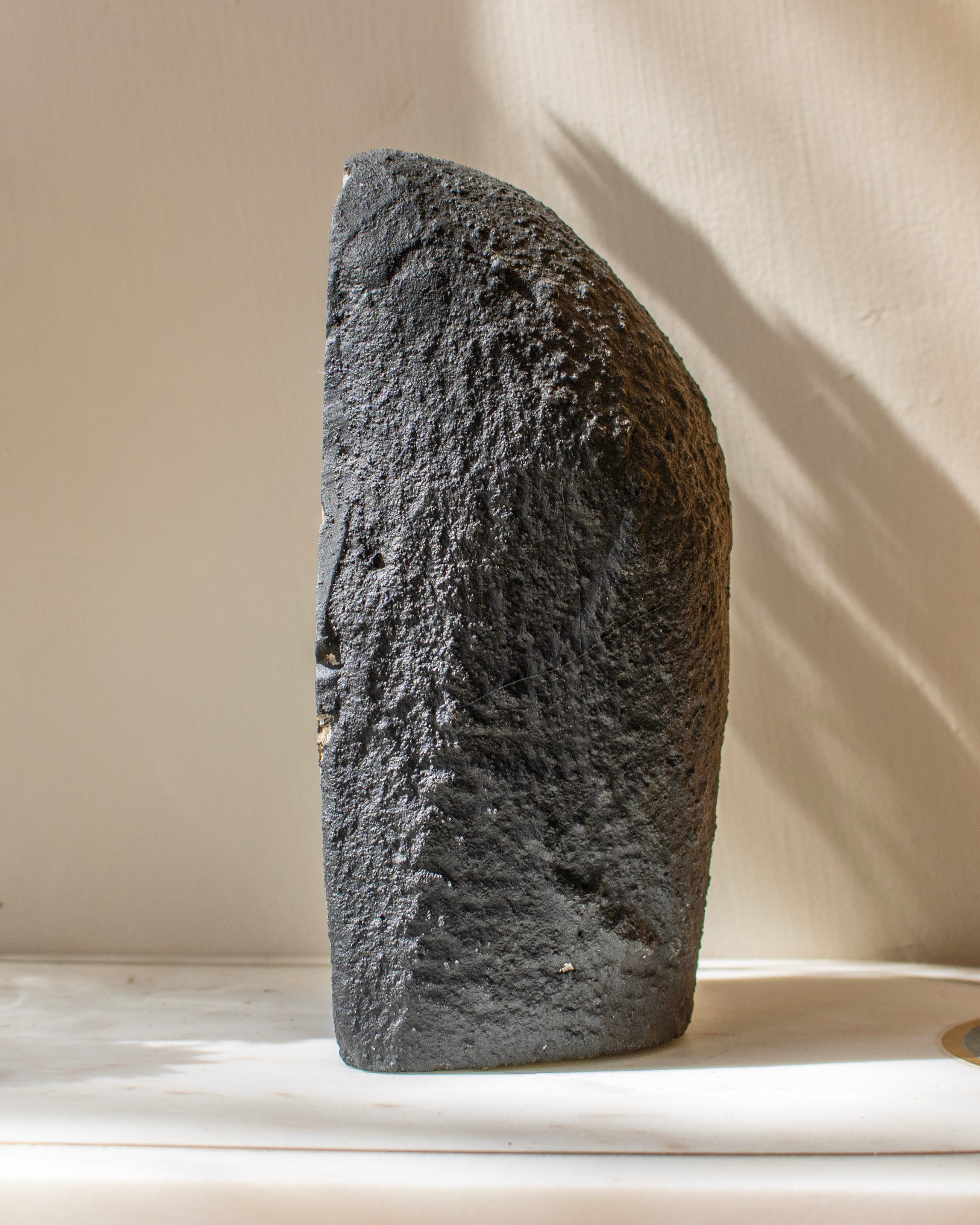 Textured black stone sculpture on a light surface with a neutral background
