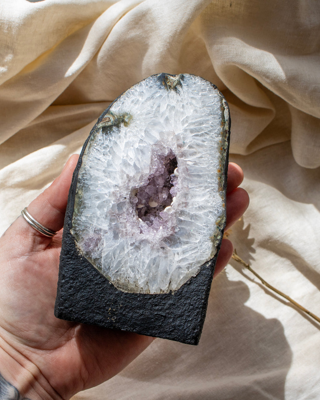 Hand holding a sliced geode with a white interior and purple center against a beige fabric background