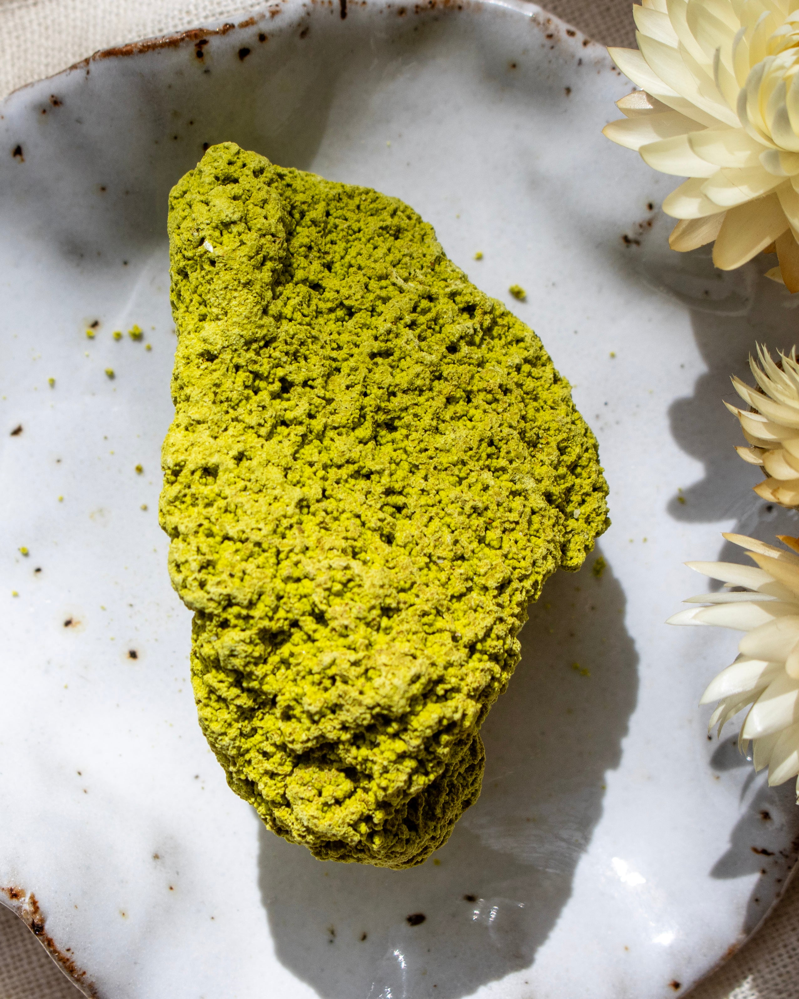 Green rock on a textured white plate with flowers