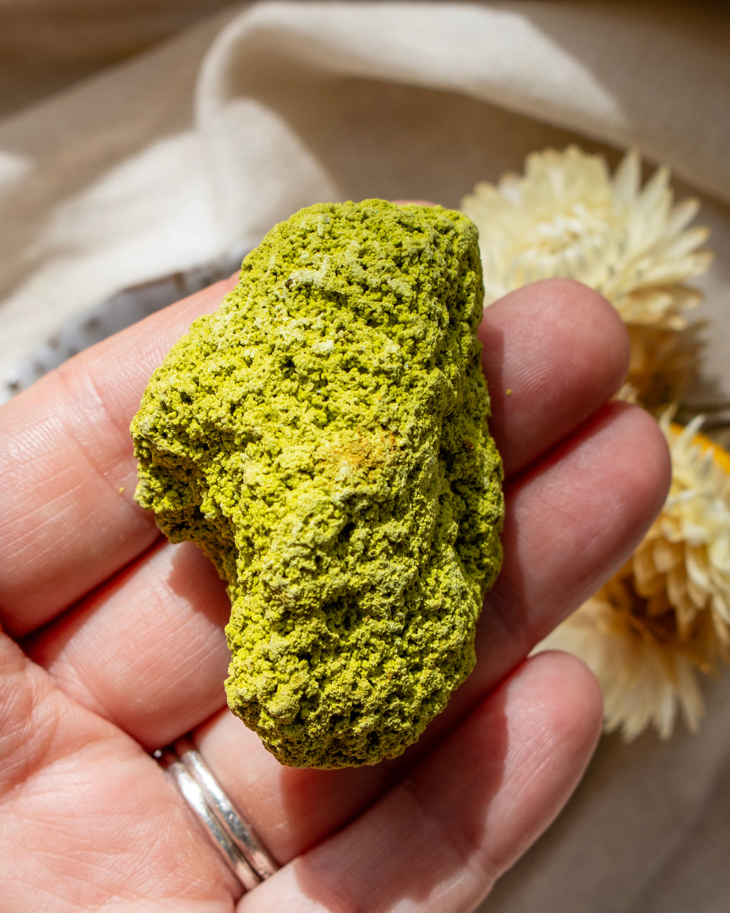 Hand holding a green rock with a beige fabric background