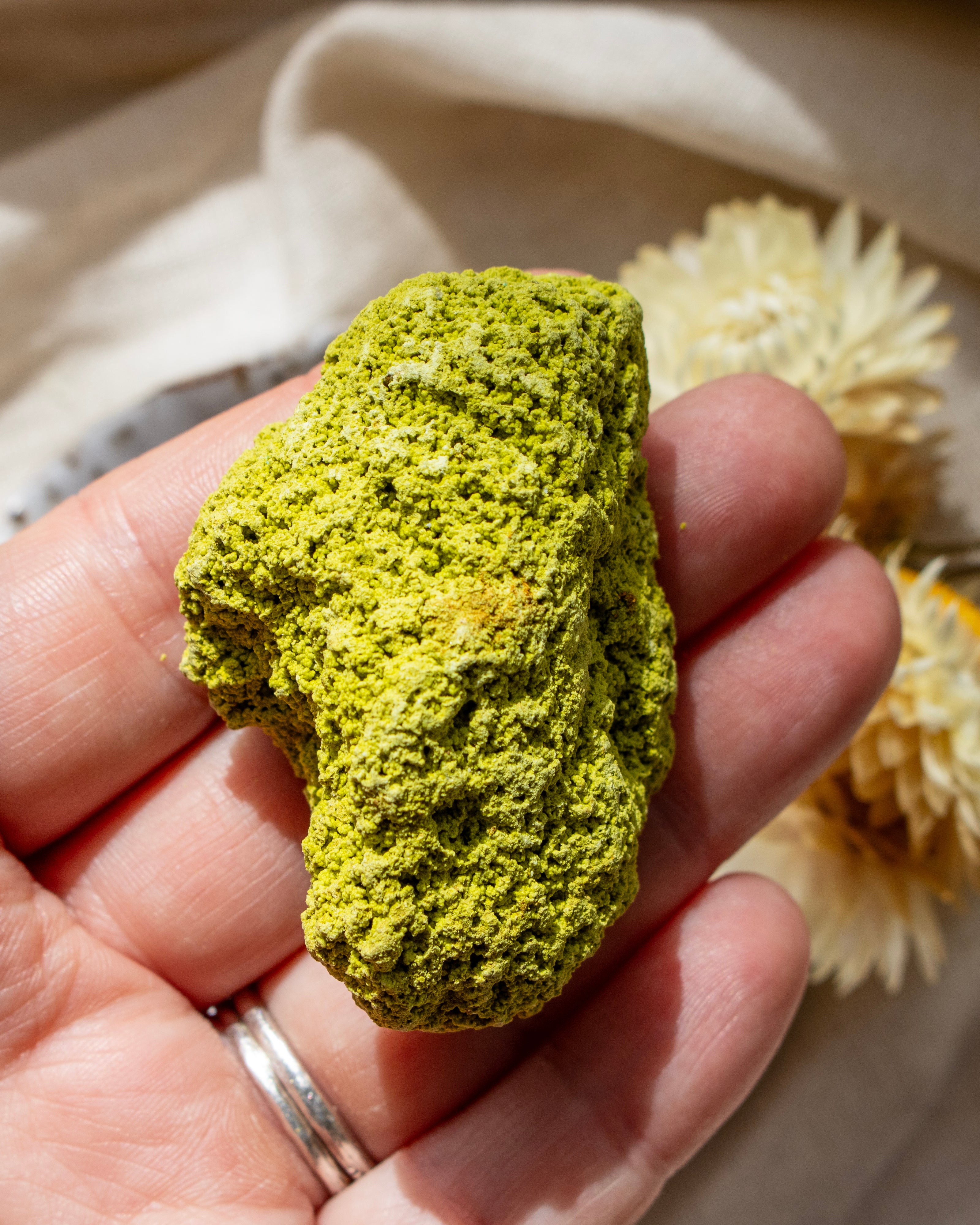 Hand holding a green rock with a beige fabric background