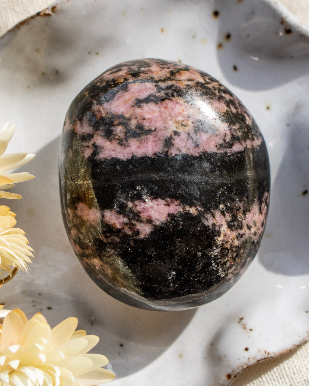 Polished rhodonite stone on a textured surface with flowers
