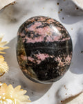 Polished rhodonite stone on a textured surface with flowers