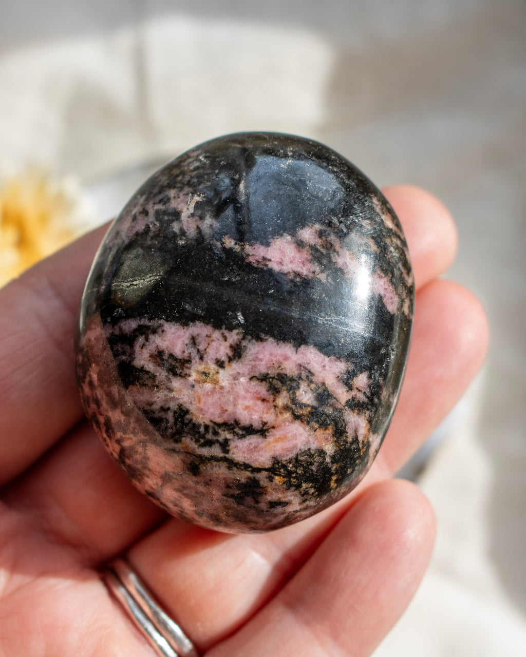 Polished rhodonite stone held in a hand with a blurred background