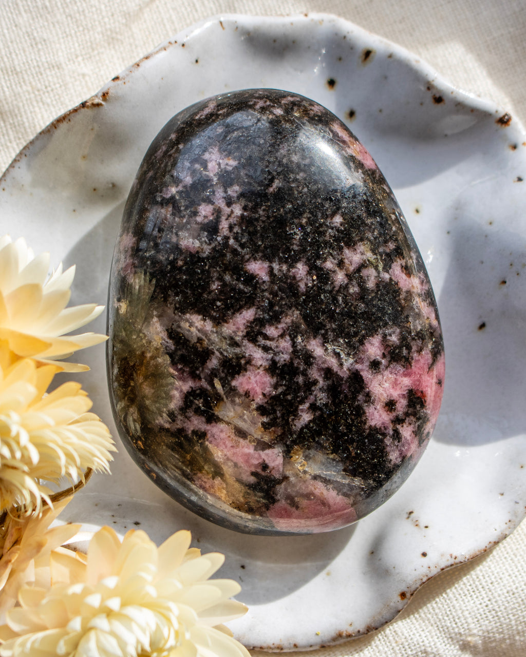 Polished rhodonite stone on a textured surface with flowers
