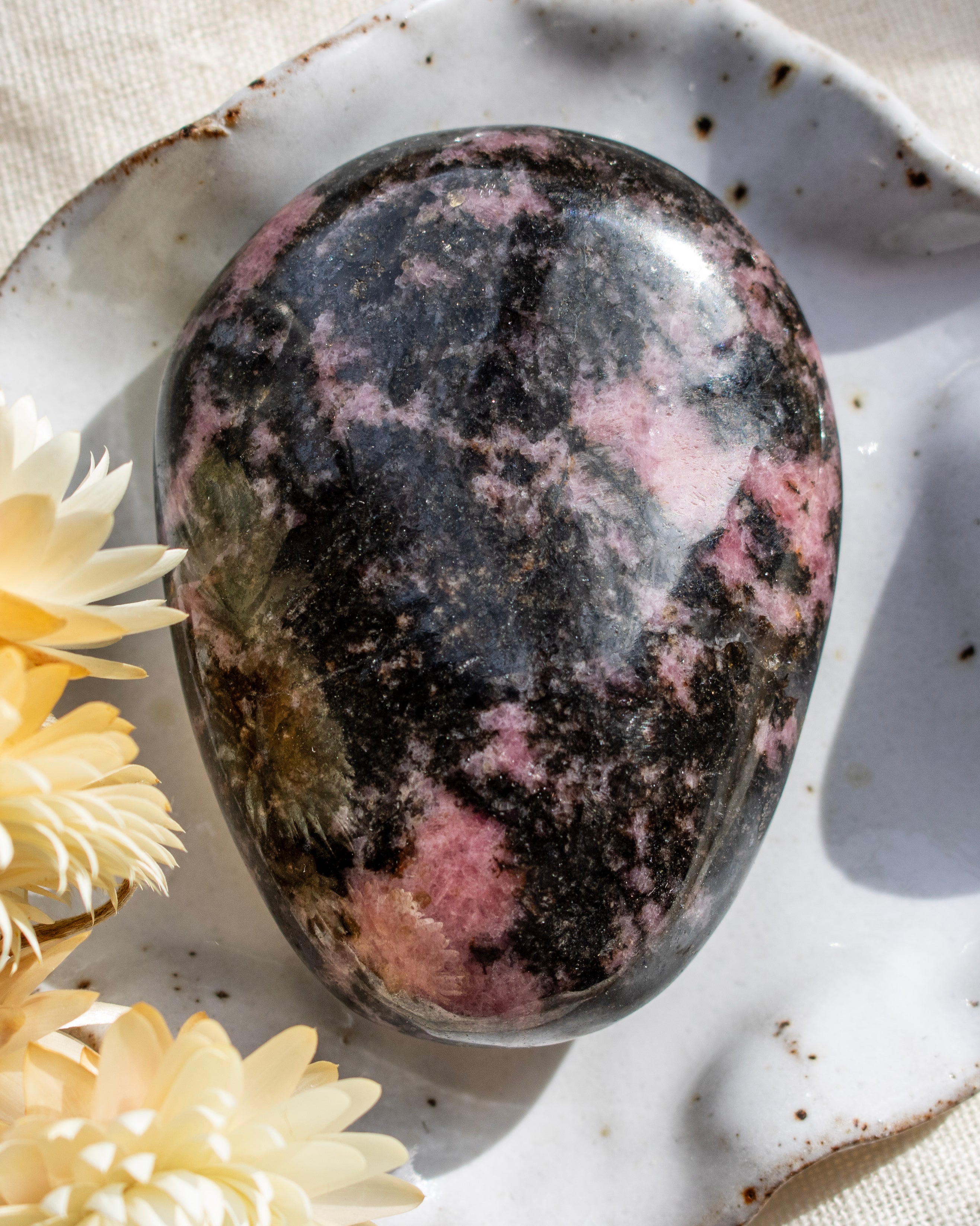 Polished rhodonite stone on a textured surface with flowers