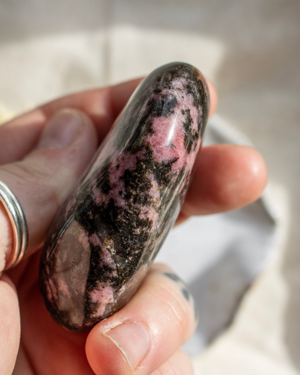 Hand holding a polychrome rhodonite stone with pink and black patterns.