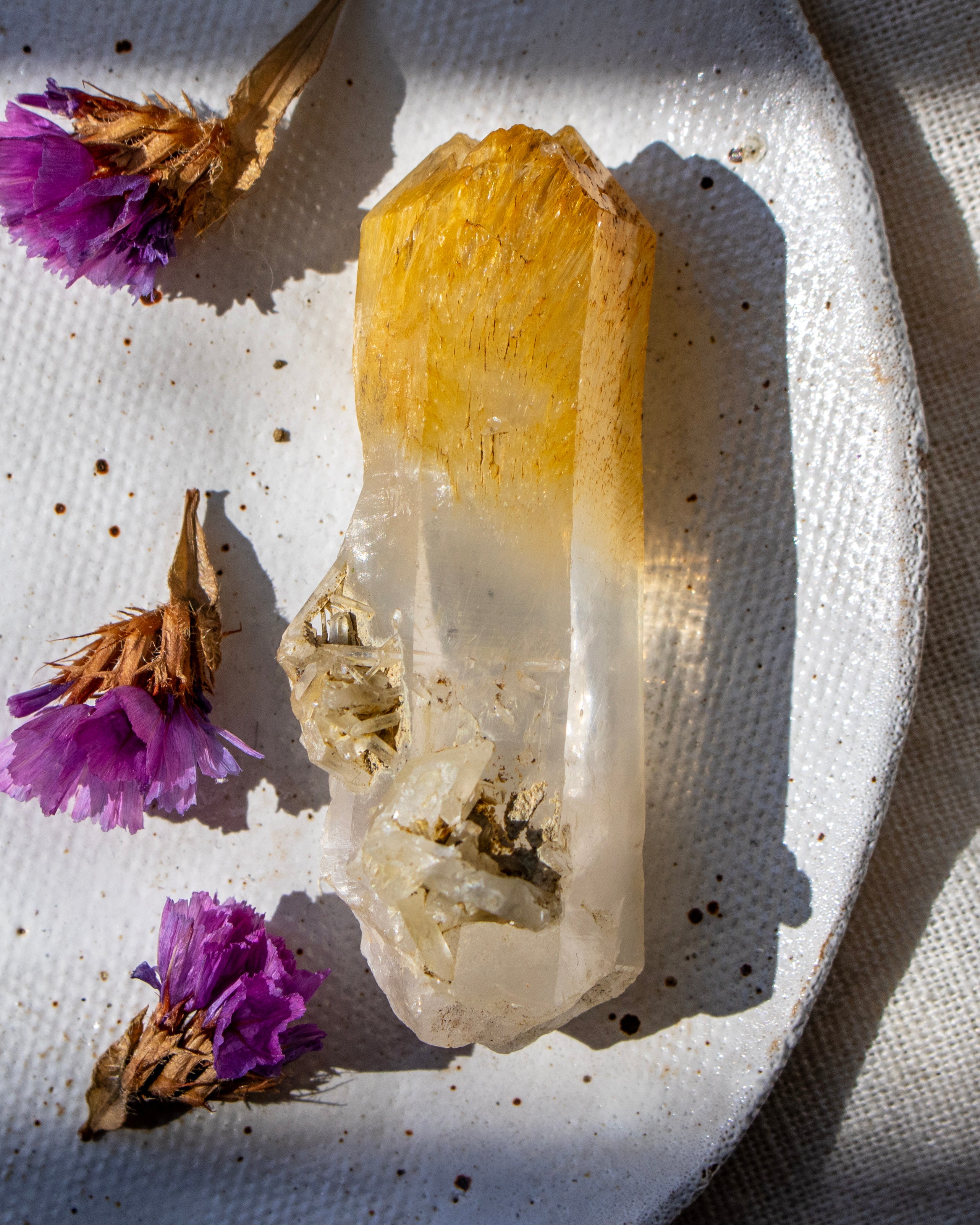 Crystal with a yellow top and white base on a textured surface with purple flowers.