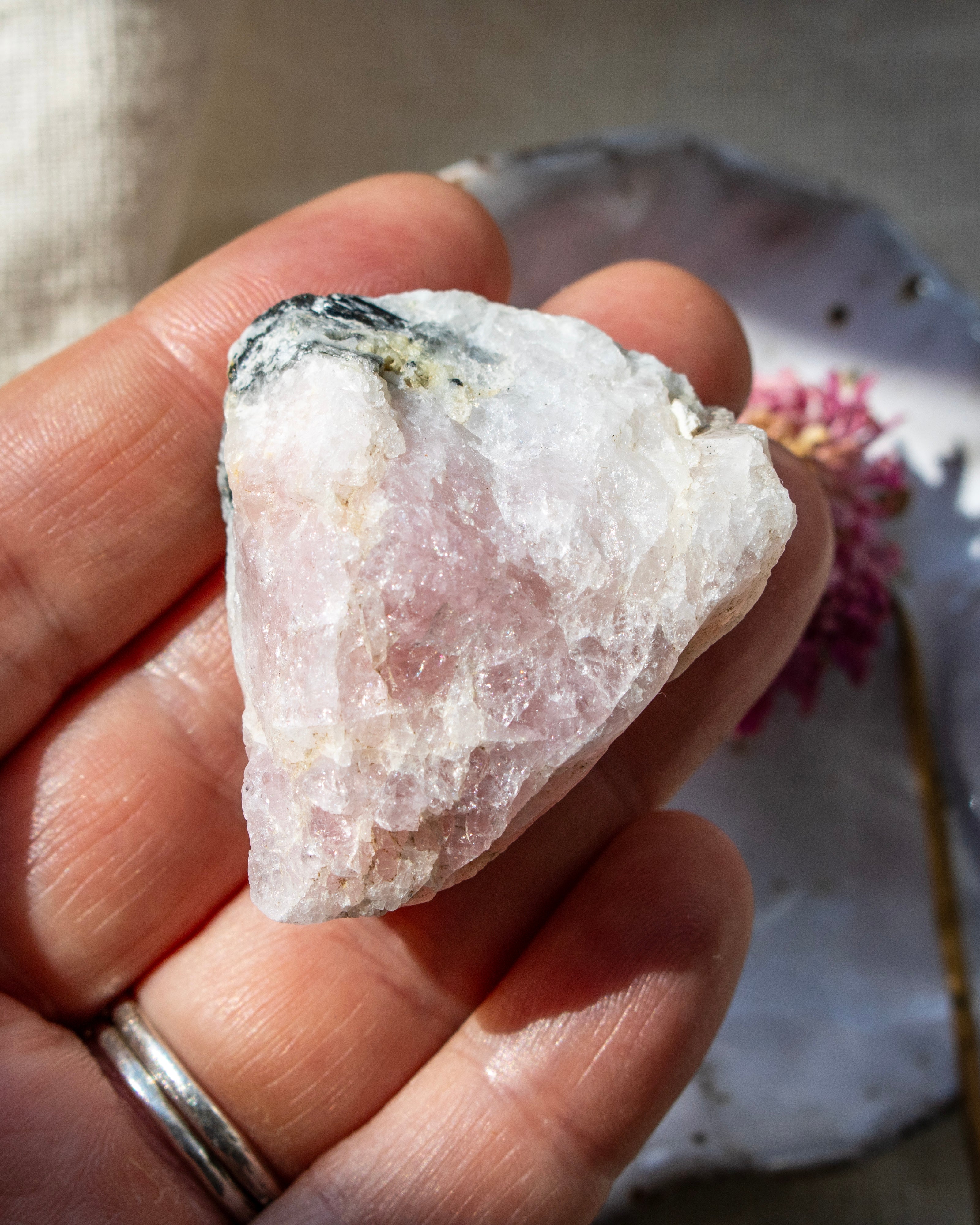 Hand holding a rough pink crystal with a blurred background